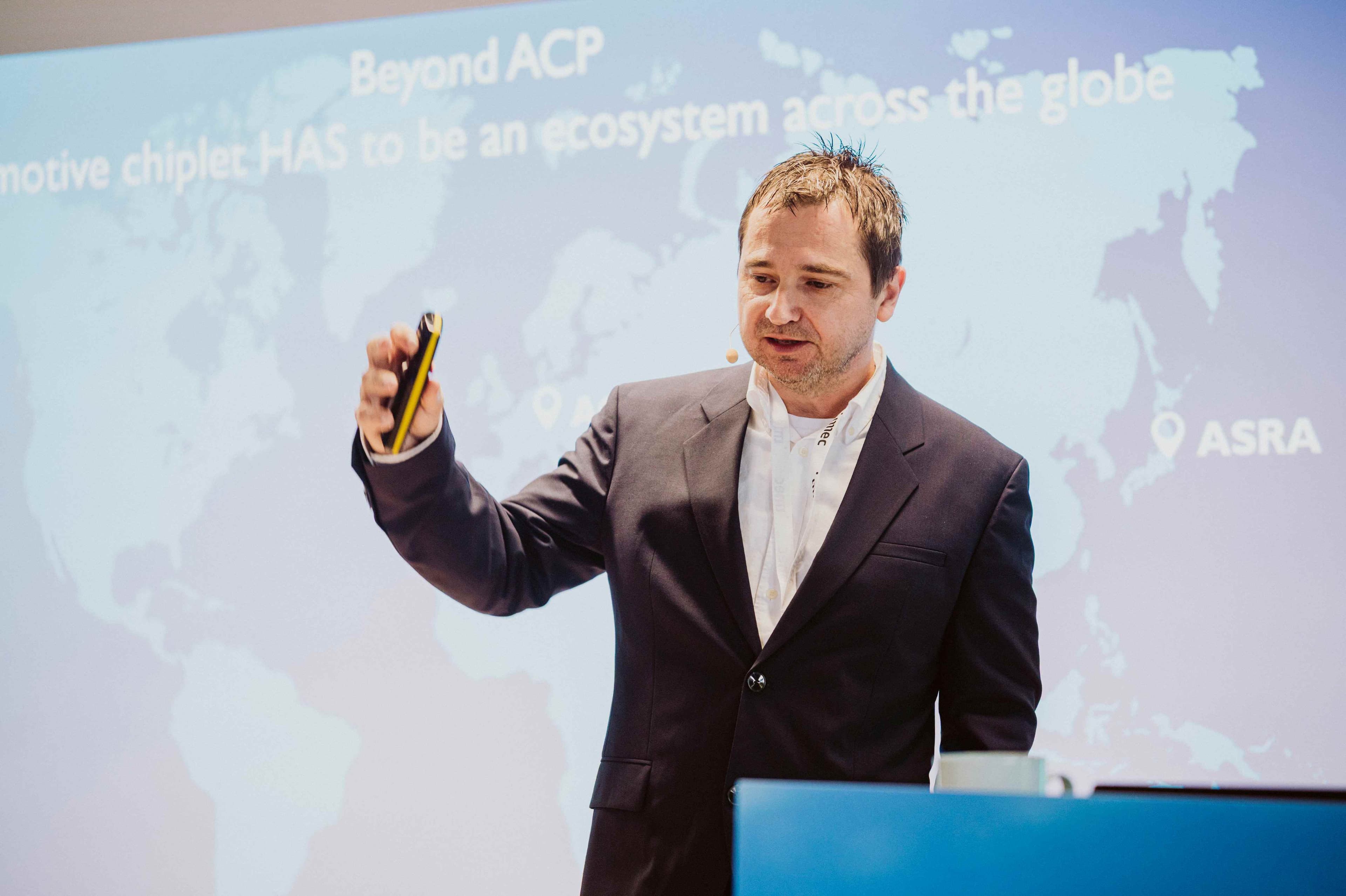 Imec%20ACF%20Fall_5 Conference speaker in a dark suit presenting with a remote in front of a chiplet roadmap slide.