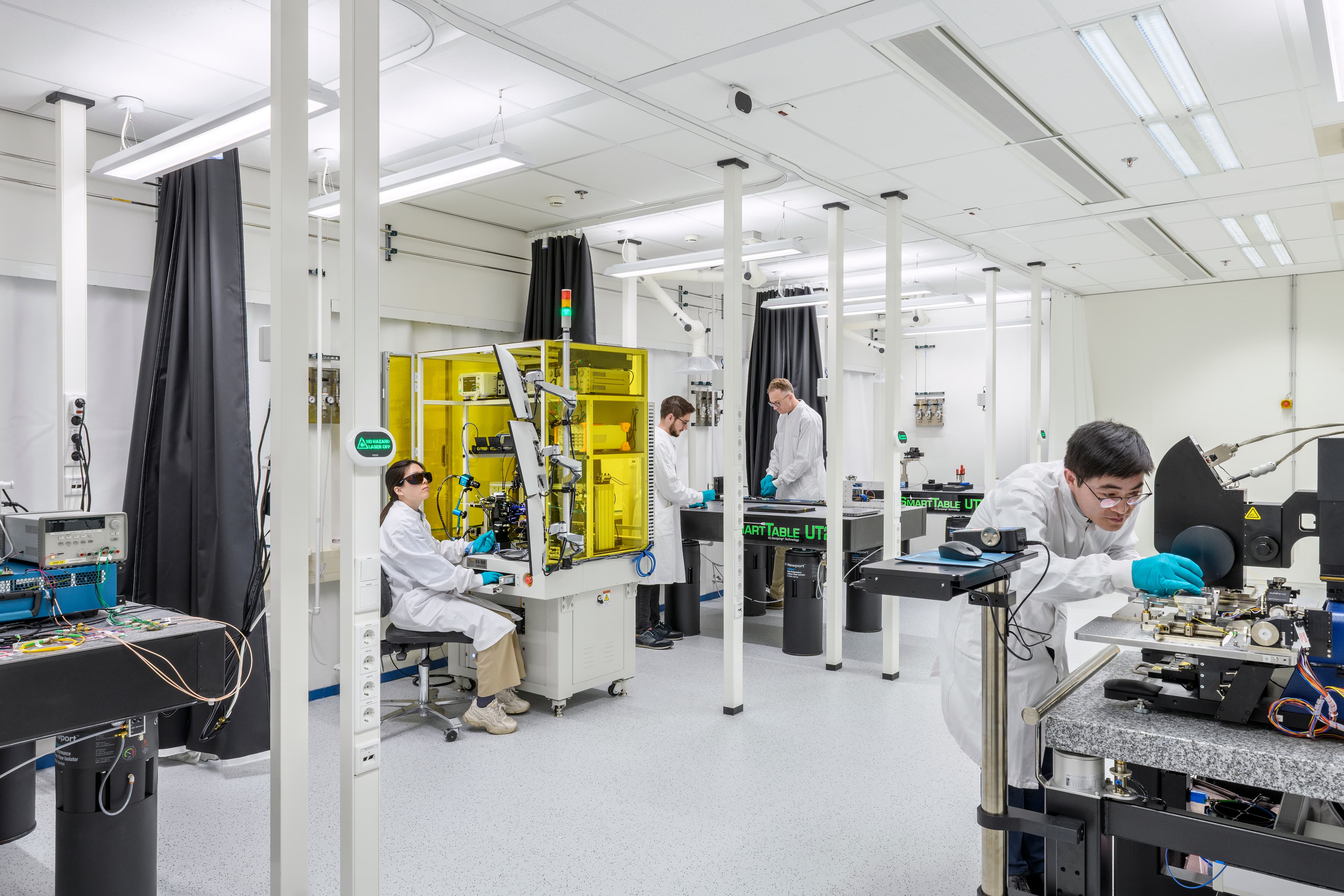 imec%20fotonica-lab%2C%20High%20Tech%20Campus%20Eindhoven Researchers in a photonics lab work with laser and optical equipment in a cleanroom-style room.