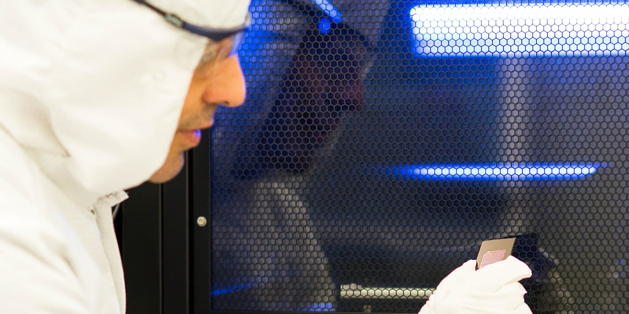 imec-graphene_1 Cleanroom researcher in protective suit examines a small graphene sample behind a hexagonal mesh screen