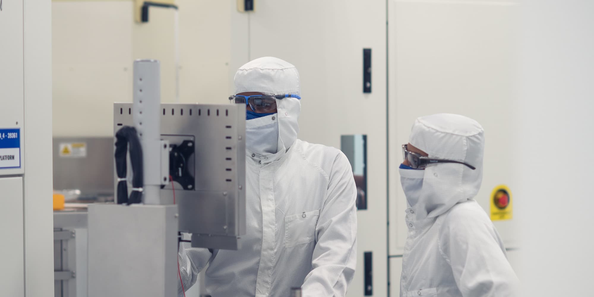 Imec-Introduces-Intermetallics-and-Airgaps-in-Advanced-Interconnect-Metallization-Schemes Two cleanroom researchers in protective suits work beside semiconductor equipment
