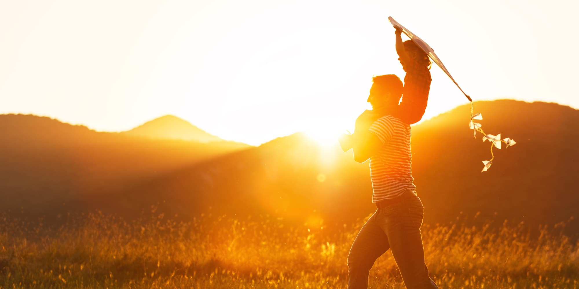 imec-magazine-0218-batteries_1 Silhouetted adult carrying a child on their shoulders in a sunlit field at sunset.