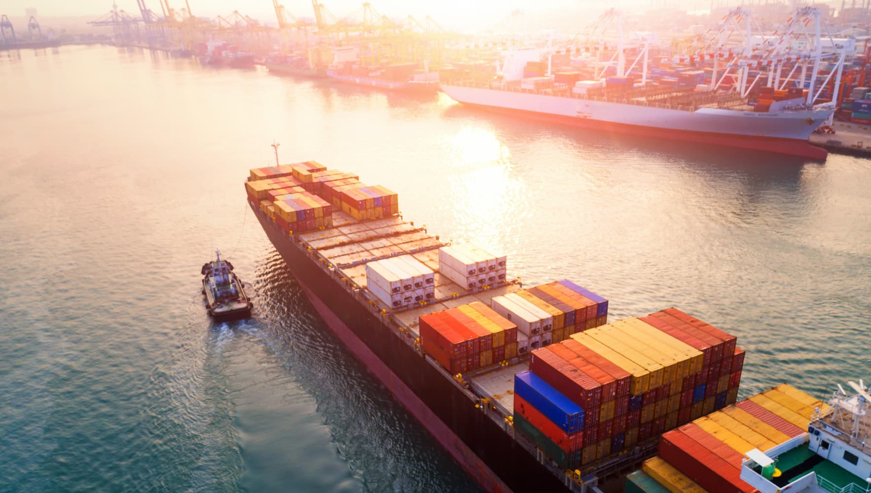 imec-magazine-ai-special-20_nieuws_1 Cargo ship loaded with stacked containers sailing through a busy port at sunrise