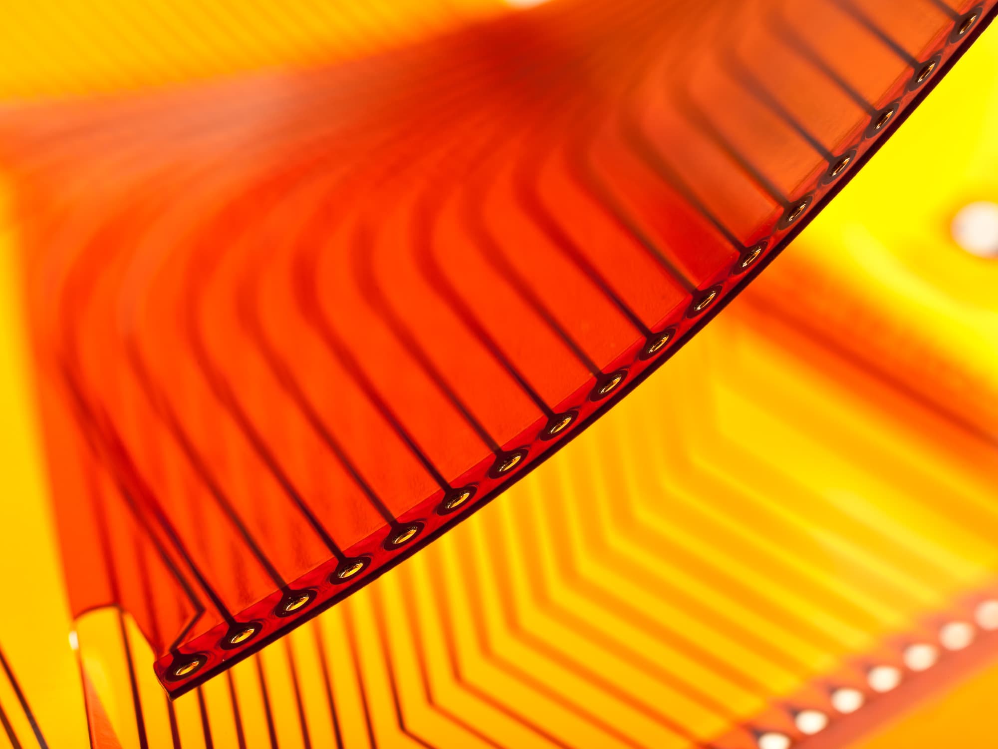 imec-magazine-flexible-electronics_1 Abstract close-up of a flexible orange-red electronic film against a bright yellow background