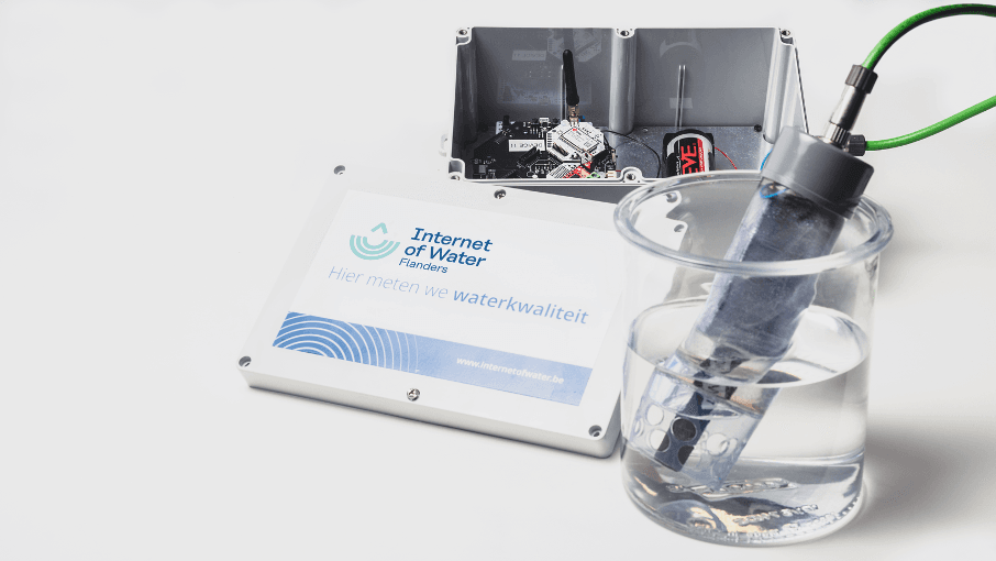imec_sensor_iow Water-quality sensor in a beaker beside a connected measuring station labeled Internet of Water Flanders