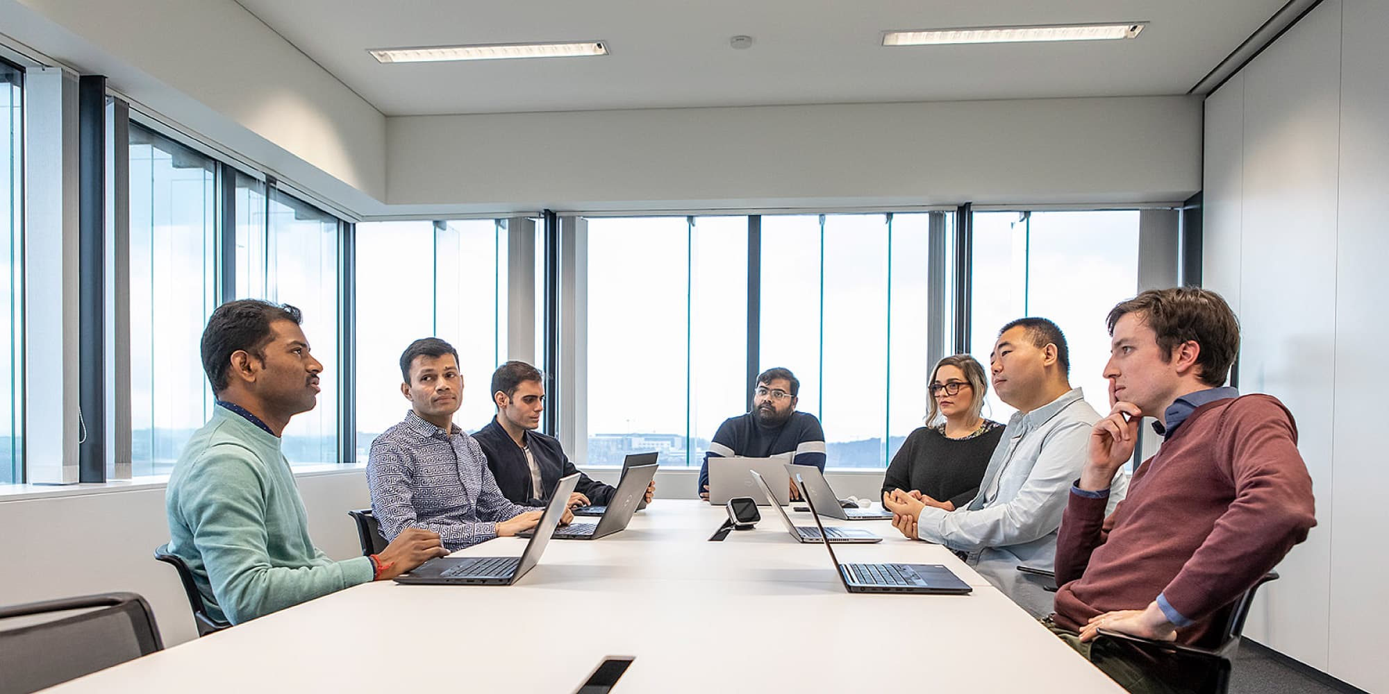 imec-spin-offs Group of eight people in a meeting room with laptops, discussing a project around a conference table.