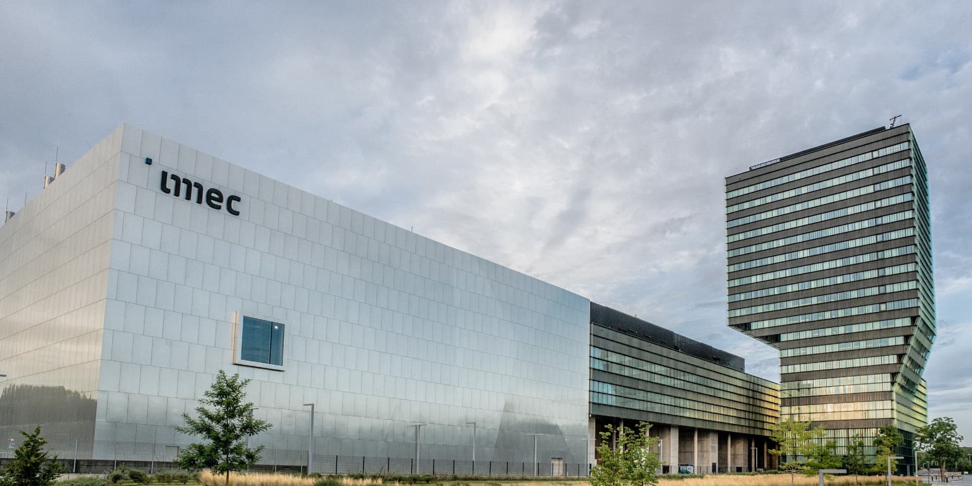 imec imec campus buildings under a cloudy sky, including a large white facility and a tall striped tower