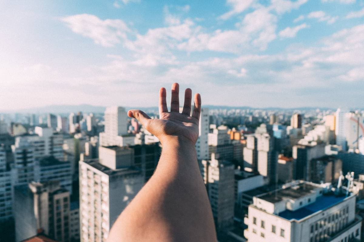 ImecCityofThings_AirQuality Hand die uitreikt naar een stadsskyline onder een wazige blauwe lucht