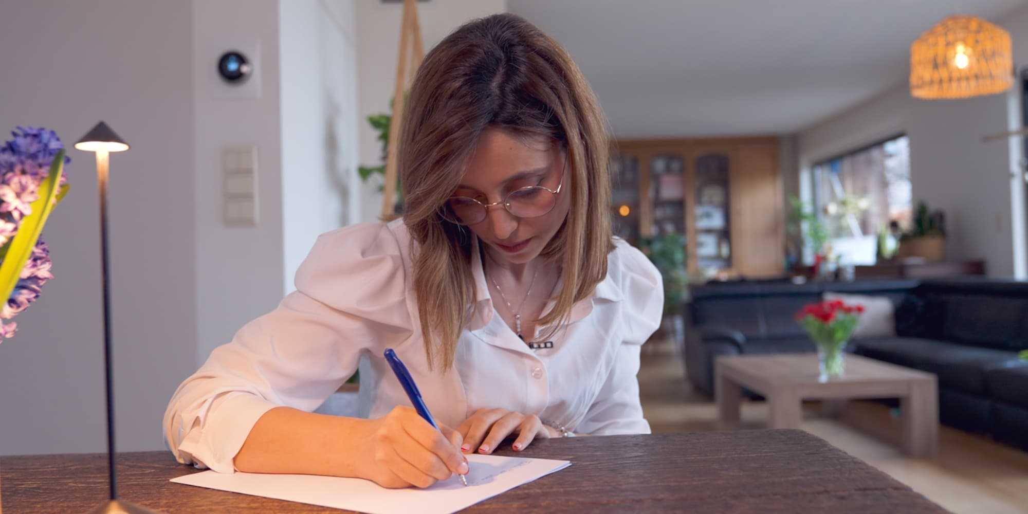 Imene-Jadli-1 Imene Jadli schrijft op papier aan een tafel in een interieur van een huis