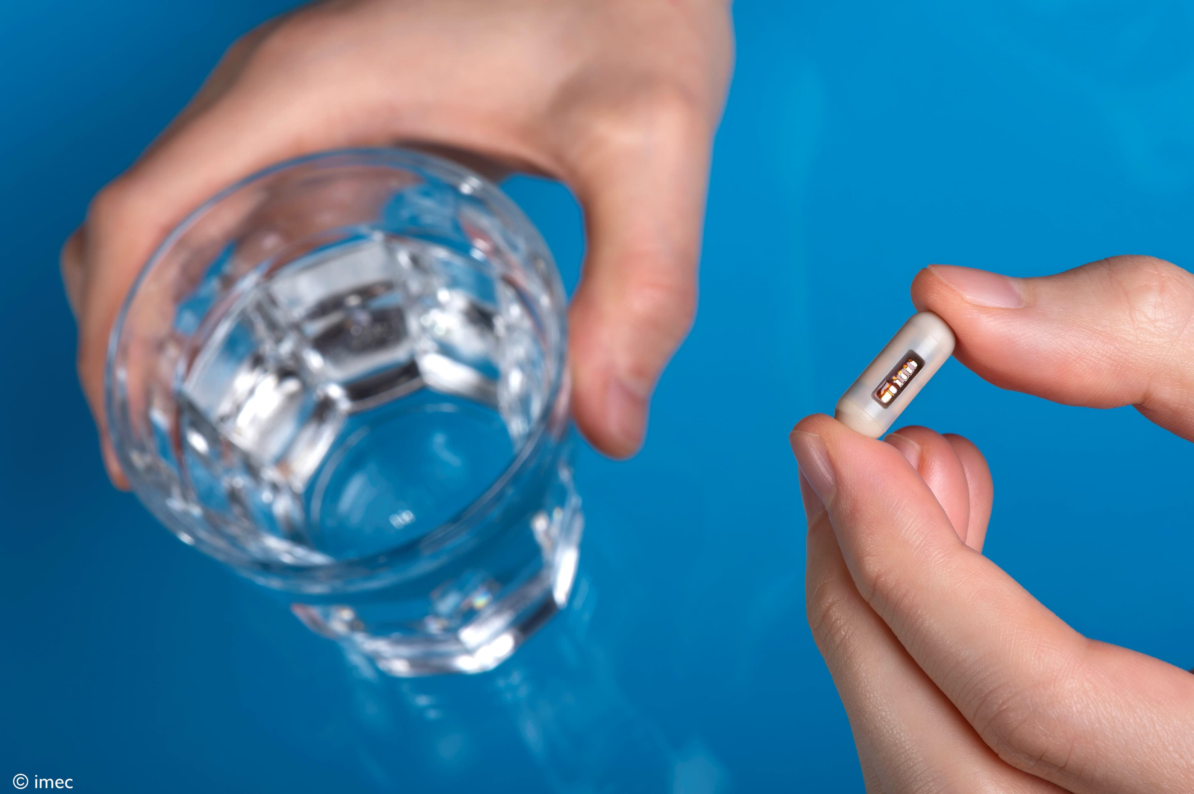 Ingestibles_header Hands holding a small ingestible sensor capsule beside a glass of water