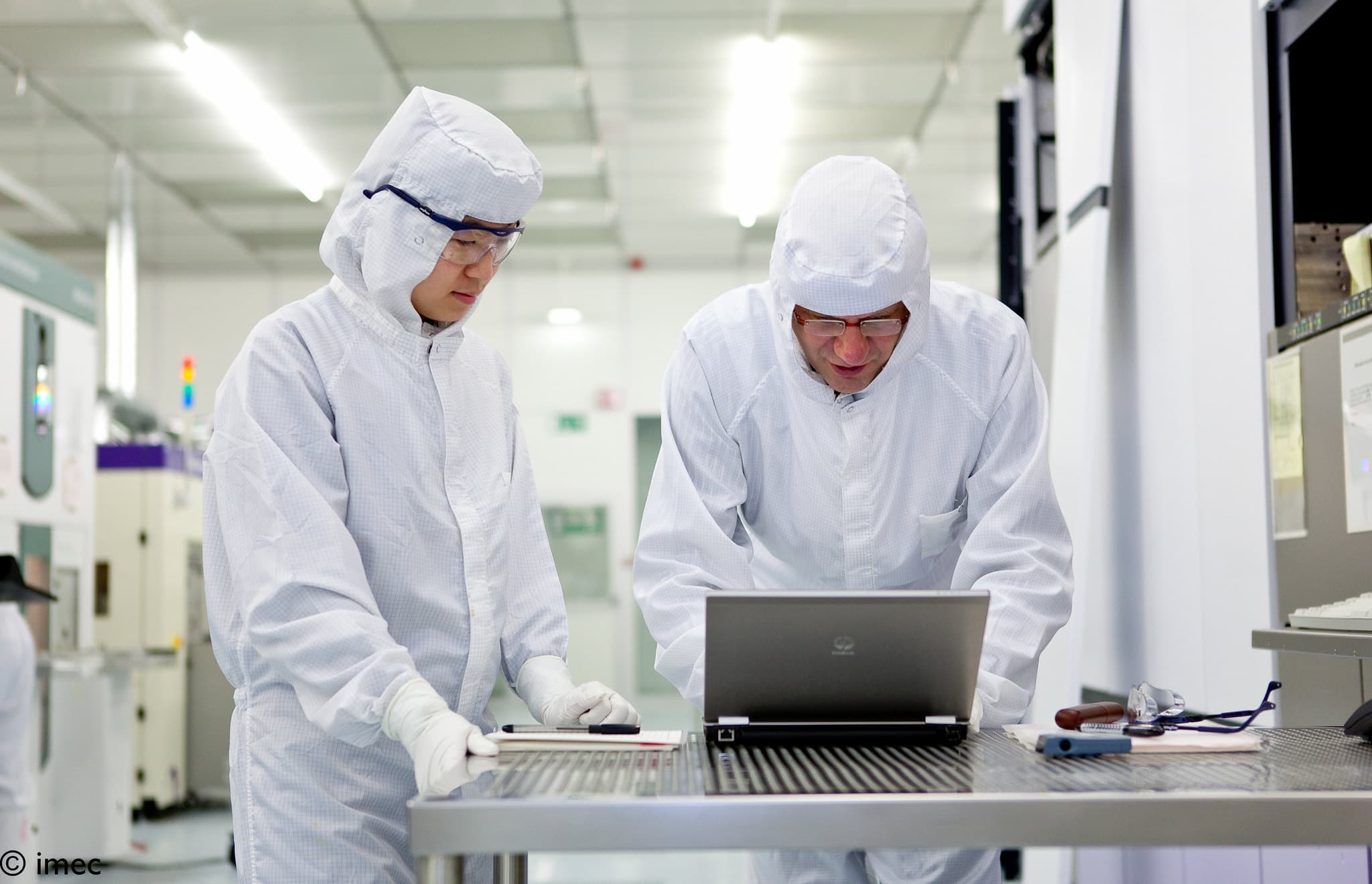 IP%20transfer Two researchers in cleanroom suits review a laptop inside a semiconductor lab
