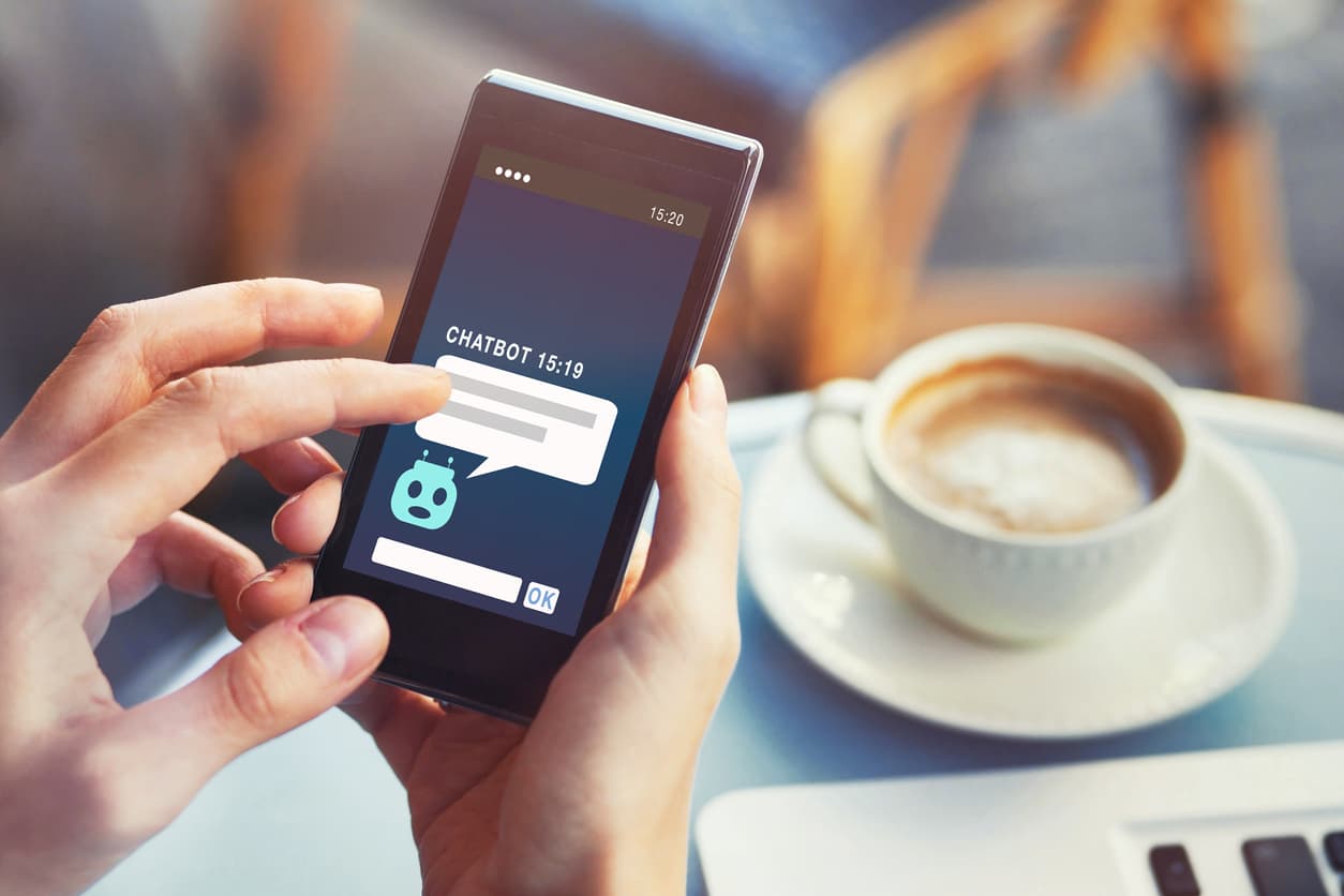 iStock-1017906110 Hands holding a smartphone showing a chatbot conversation beside a cup of coffee