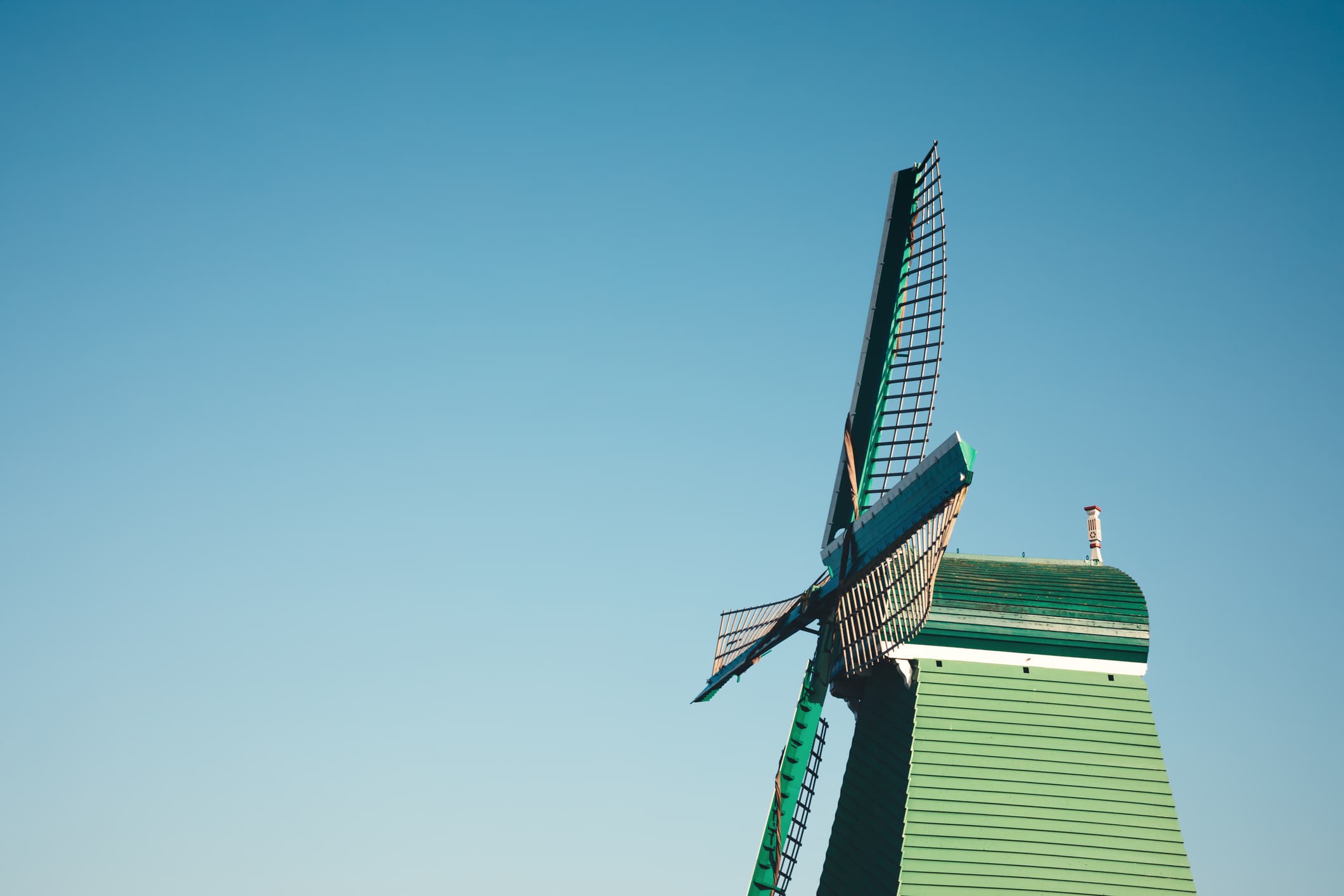 iStock-1031257984 Modern green windmill with blades against a clear blue sky