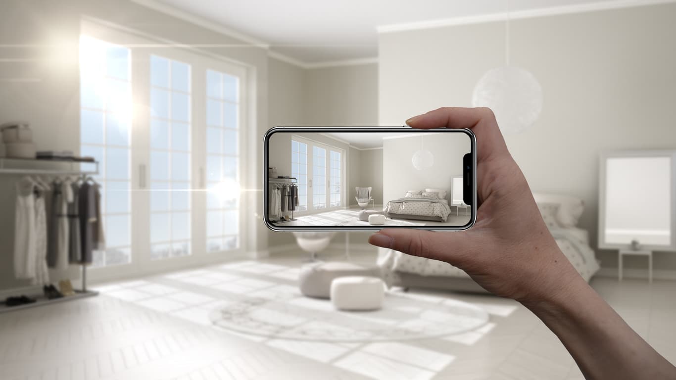 Hand holding smartphone showing augmented reality view of room Hand holding a smartphone that shows a room through augmented reality-style camera view