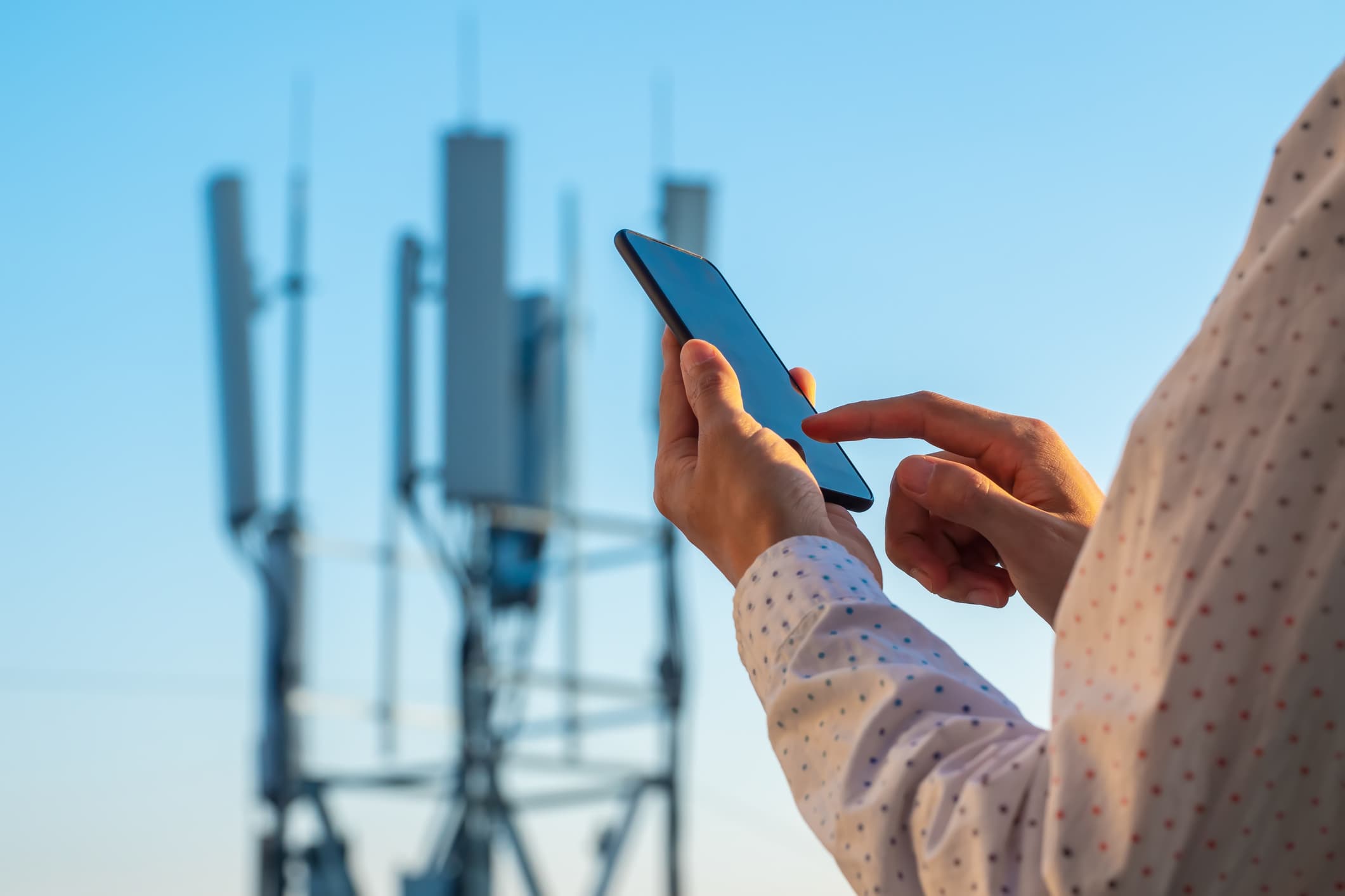 iStock-1225585631 Person using a smartphone in front of blurred 5G antenna towers