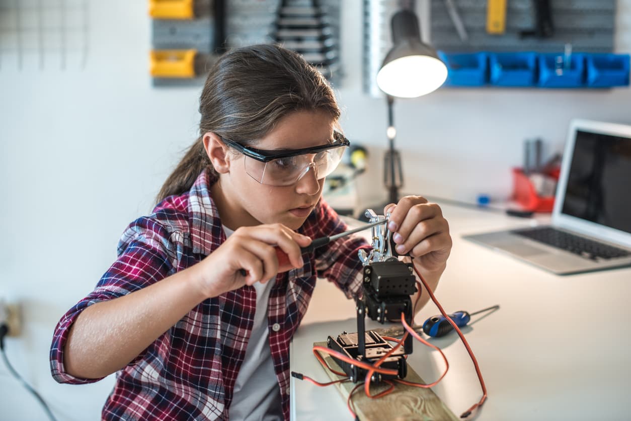 iStock-601140418 Jong meisje met veiligheidsbril zet een kleine robot in elkaar aan een werkbank