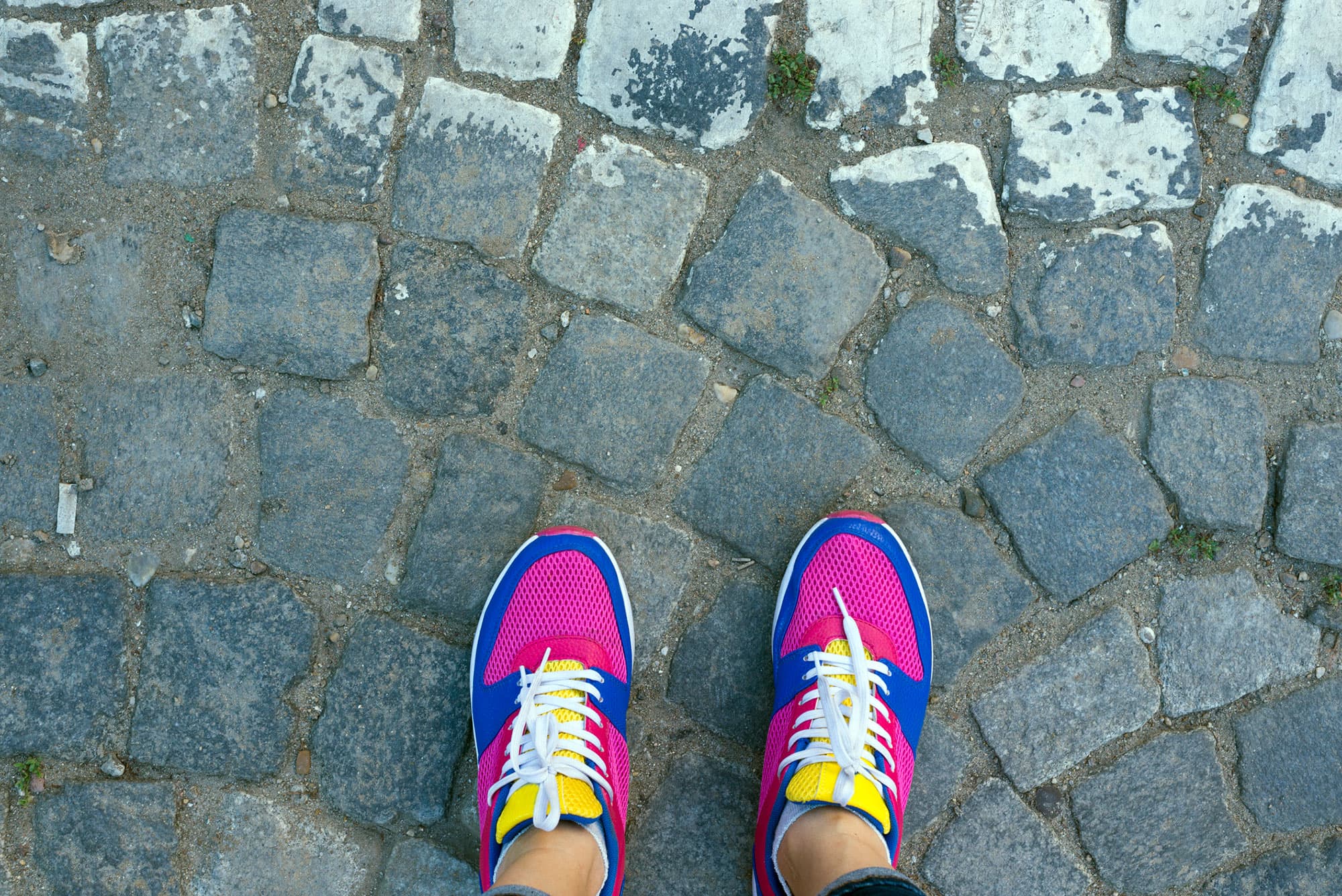 Colorful running shoes on cobblestone path Overhead view of colorful running shoes on a cobblestone path