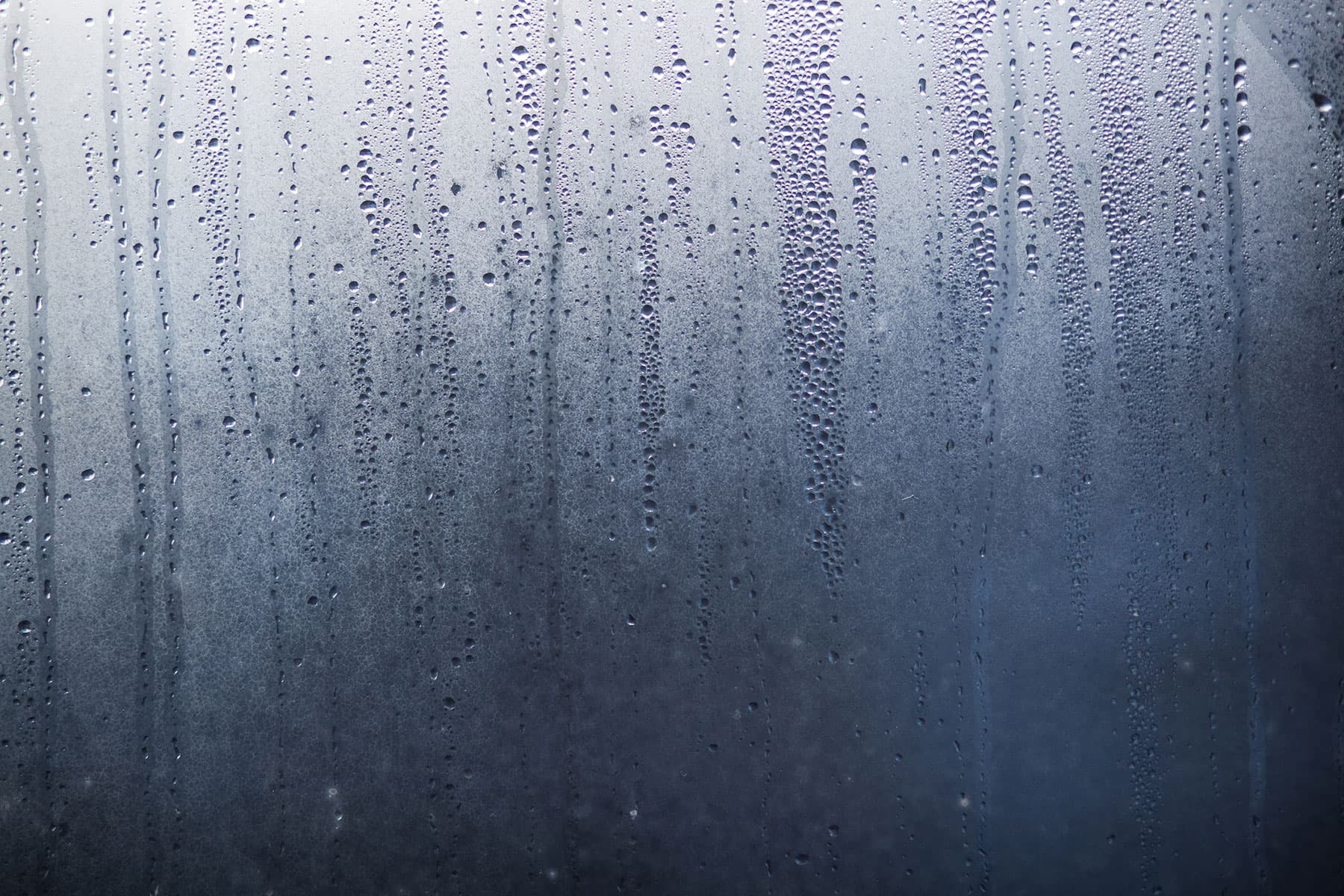 Condensation droplets on fogged glass Condensation droplets streak across a fogged glass surface, evoking a moody, rainy atmosphere.