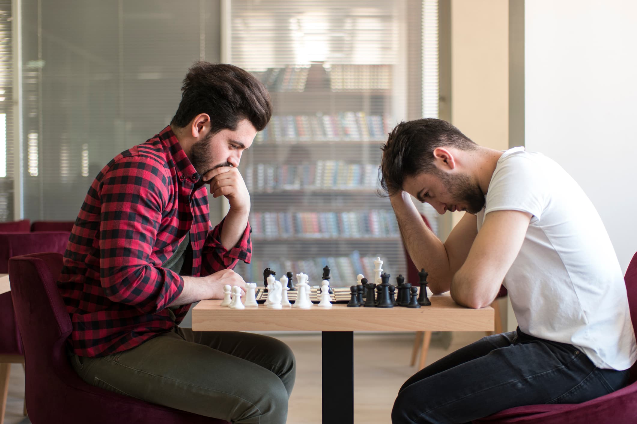 iStock-938491902 Two young men lean over a chessboard, concentrating on their next move.