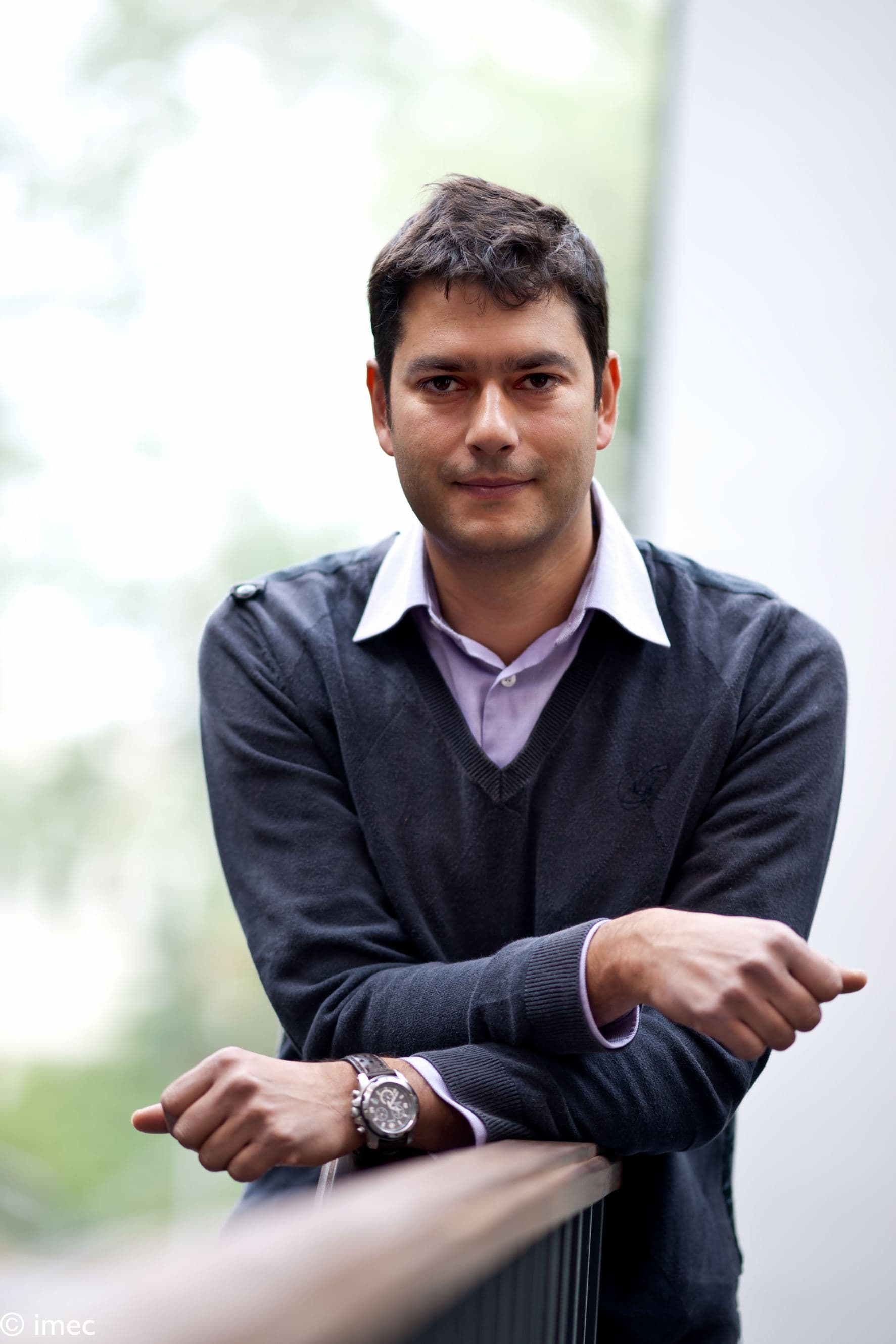 julien_ryckaert_lr_1 Portrait of Julien Ryckaert leaning on a railing, wearing a dark sweater over a collared shirt.