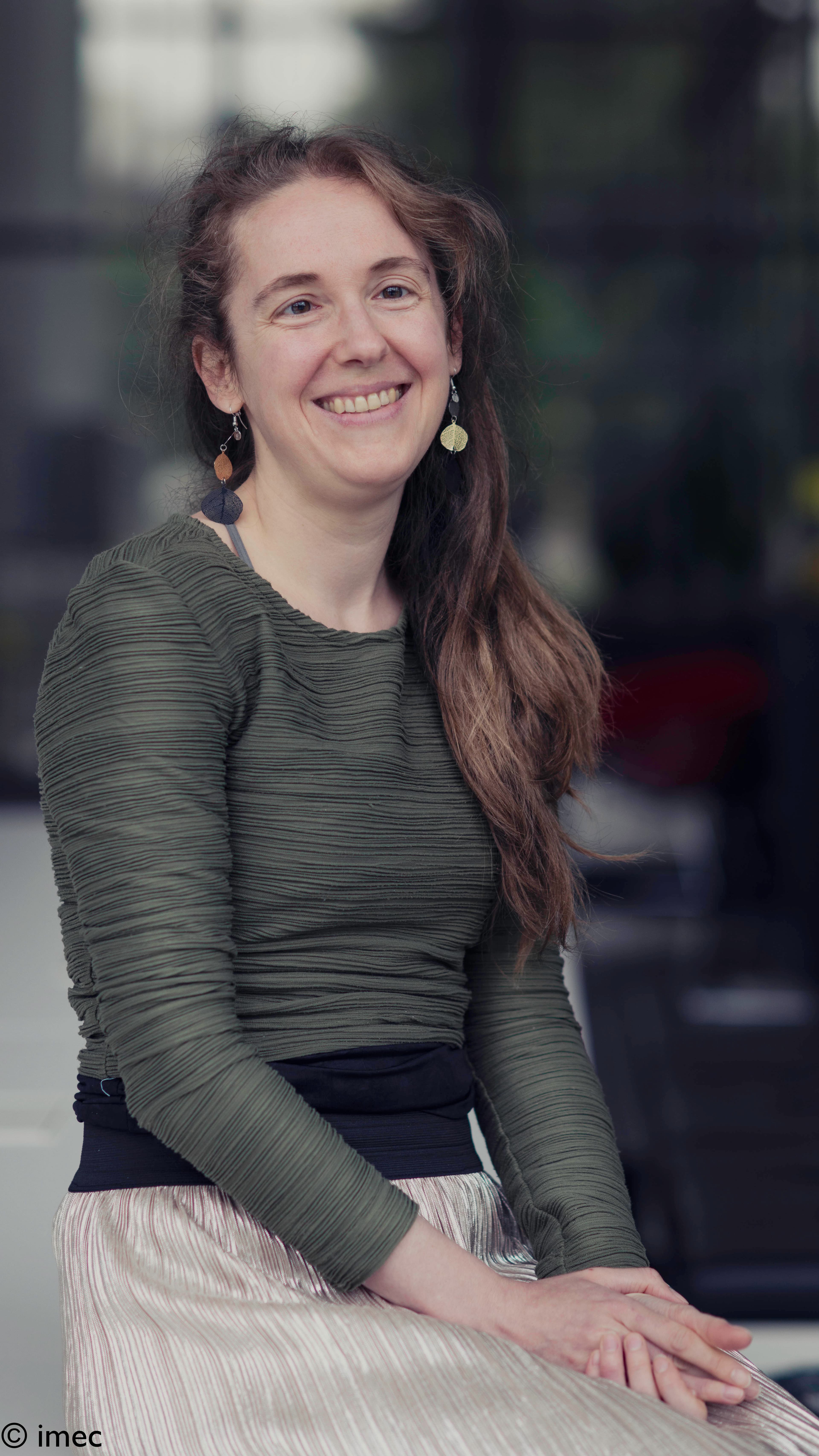 Katrien Portrait of Katrien Mols smiling in a green top, seated against a blurred background