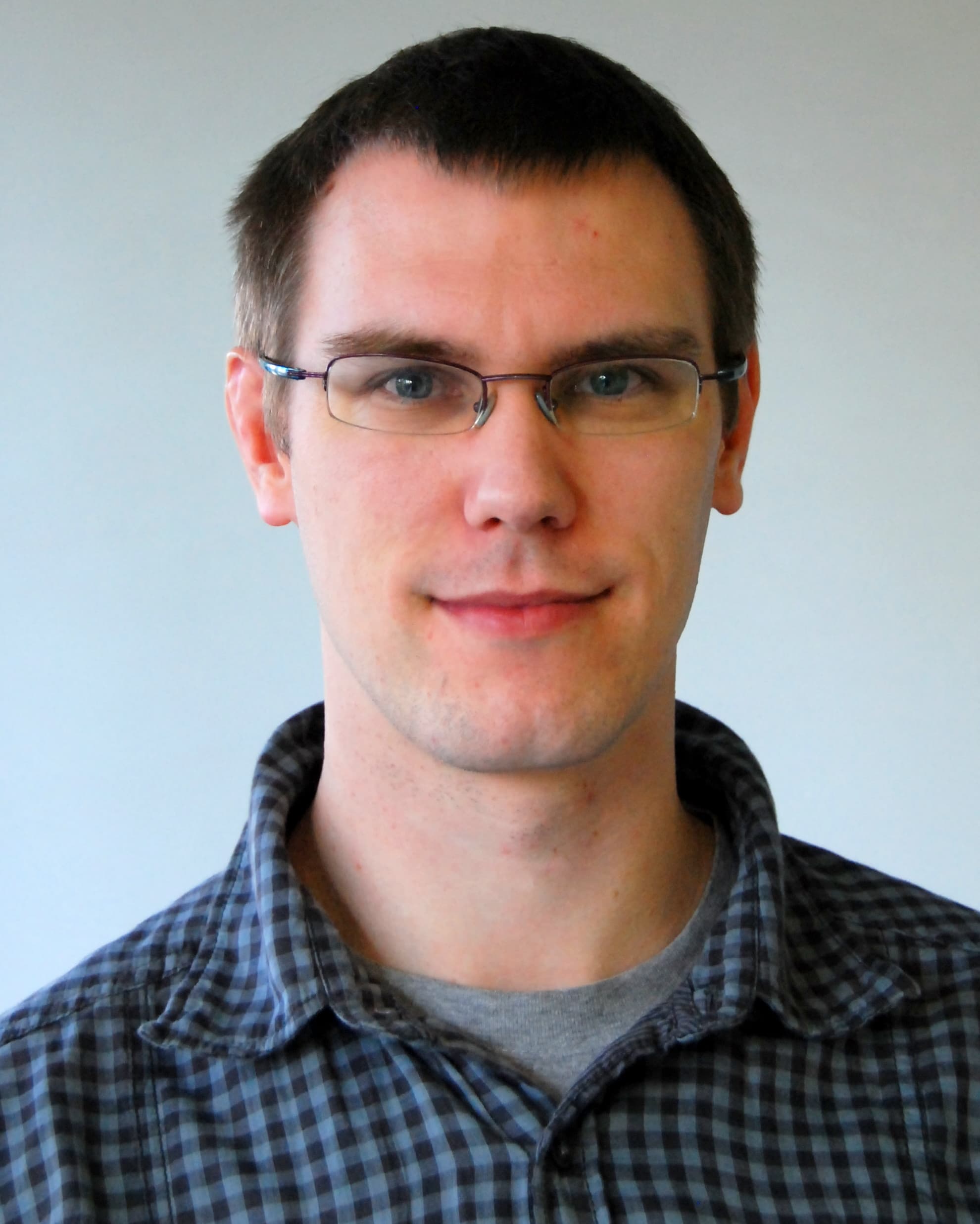 Kris_Myny_bio_1 Head-and-shoulders portrait of Kris Myny wearing glasses and a blue plaid shirt against a plain background.