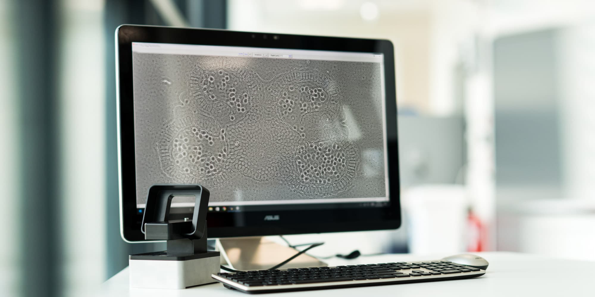 life-sciences-technology-platform-imaging_1 Desktop monitor showing a microscope image of cells beside a small lab instrument and keyboard