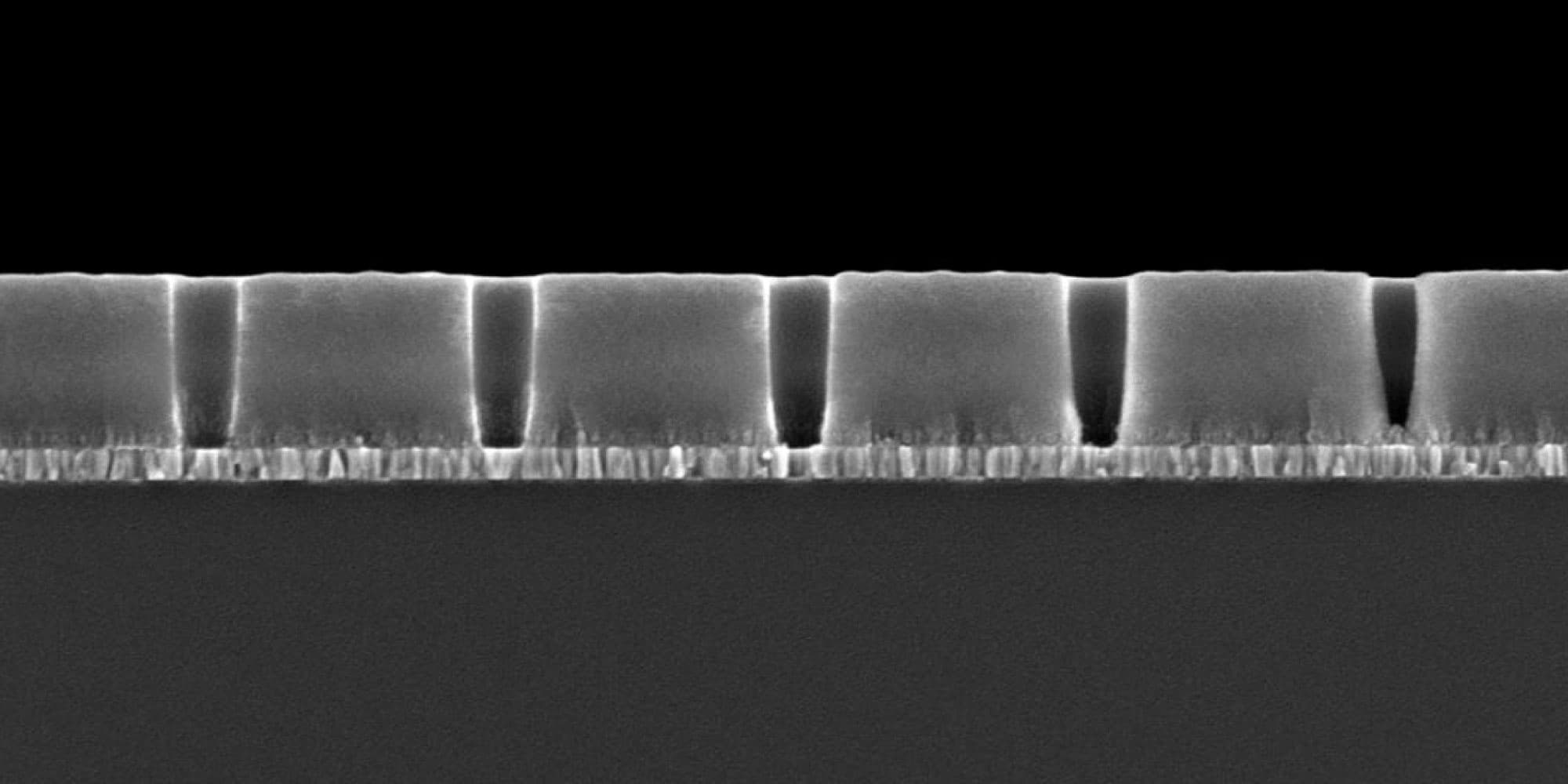 liquid-memories Microscope cross-section of layered material with repeated vertical channels, suggestive of liquid-based memory structures