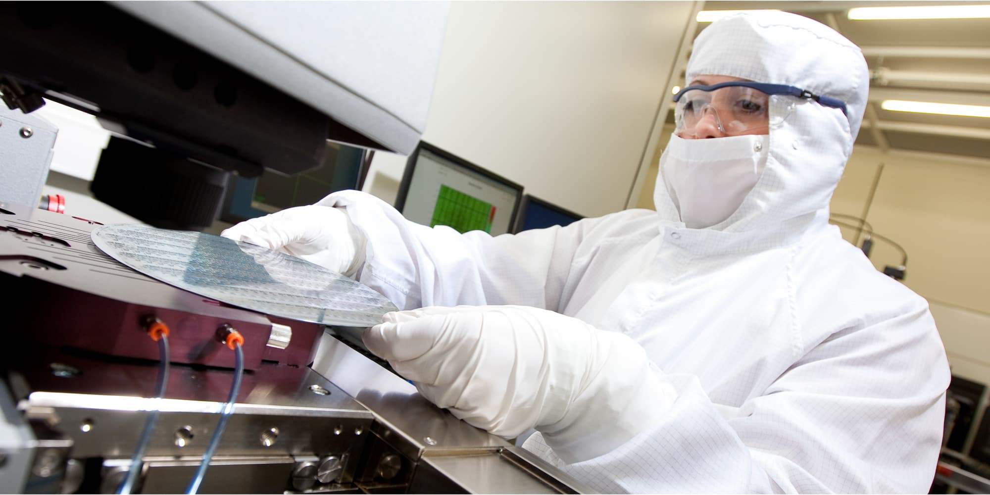 Machine-learning-accelerators Researcher in cleanroom gear handling a silicon wafer in a semiconductor lab