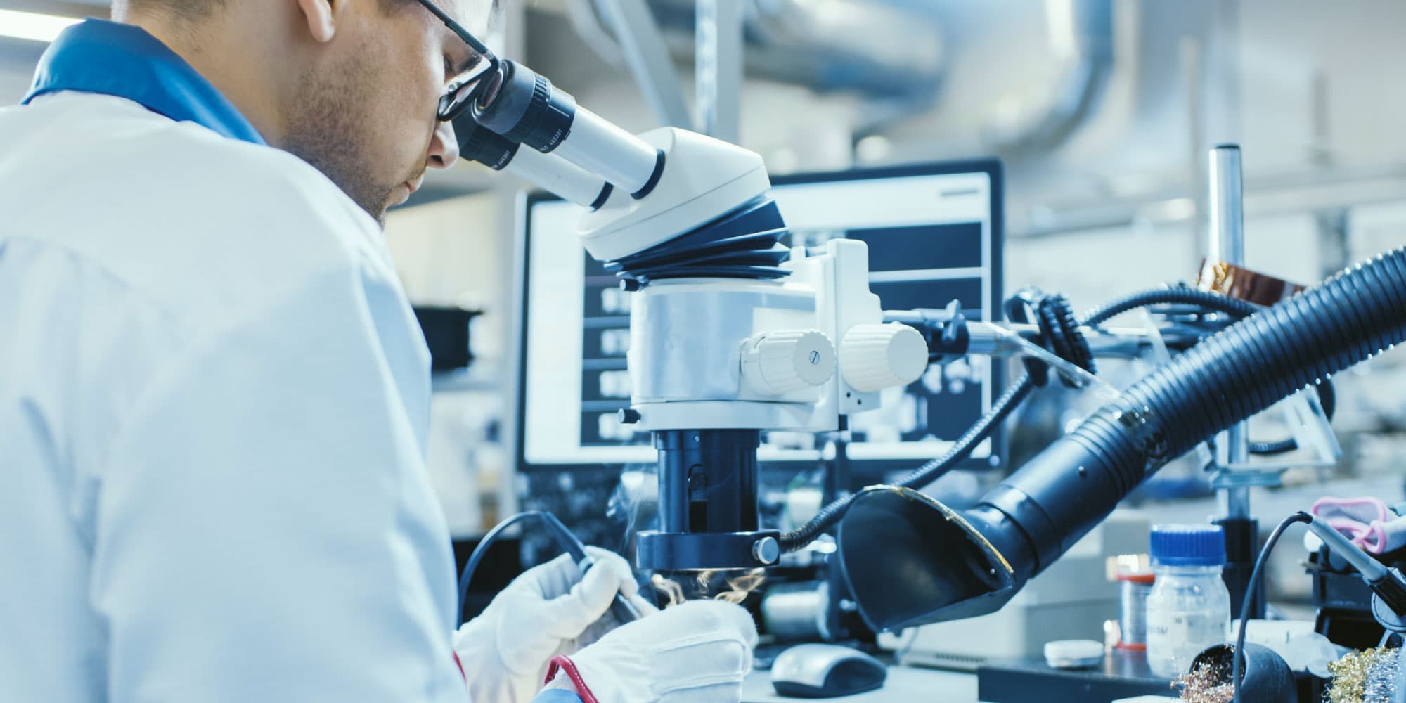 main-article-IMOMEC Researcher in a lab coat using a microscope in a materials research laboratory