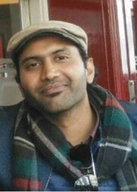Manu%20Perumkunnil Portrait of Manu Perumkunnil Komalan wearing a cap and scarf, smiling at the camera
