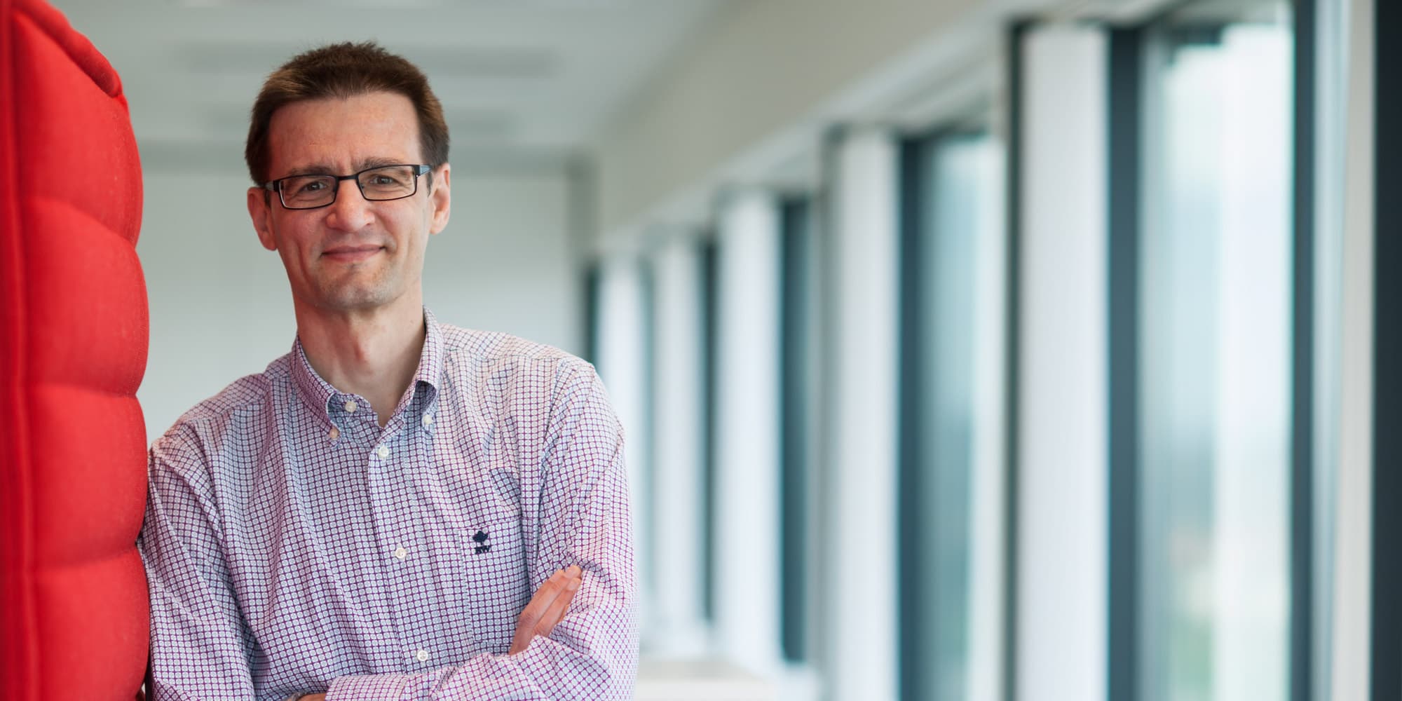 Meet-imec-fellow-Jan-Craninckx Jan Craninckx standing in a bright hallway with arms crossed