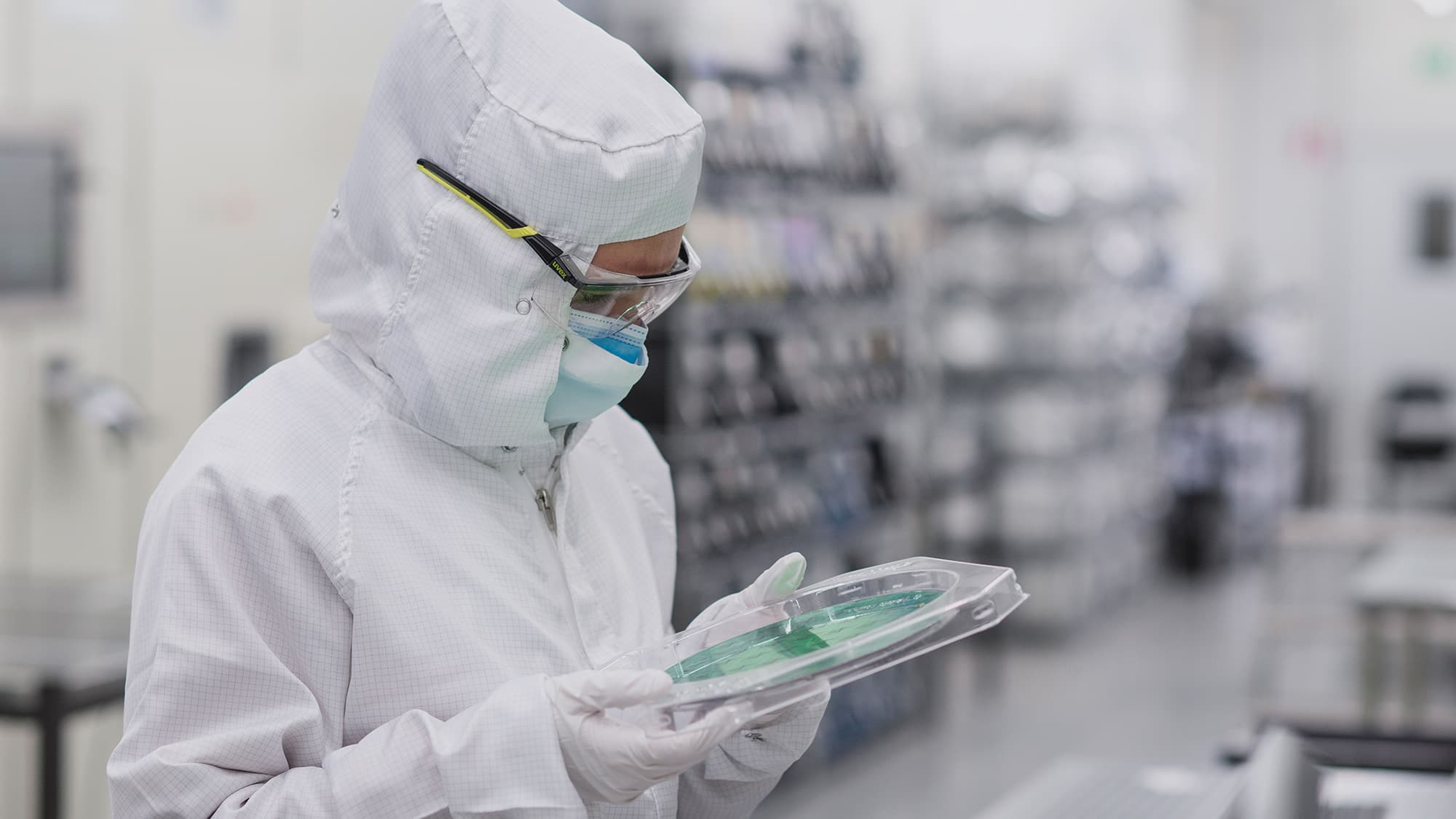 MEMS-foundry Cleanroom technician in protective suit inspecting a semiconductor wafer