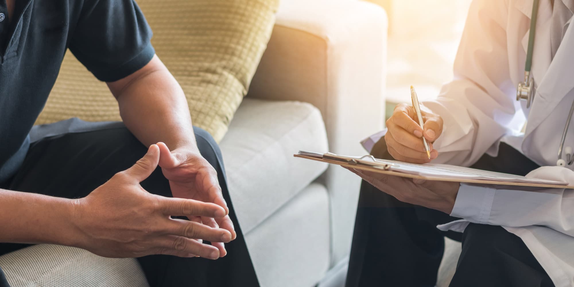 mental_health_header_1 Doctor taking notes while speaking with a seated patient during a consultation