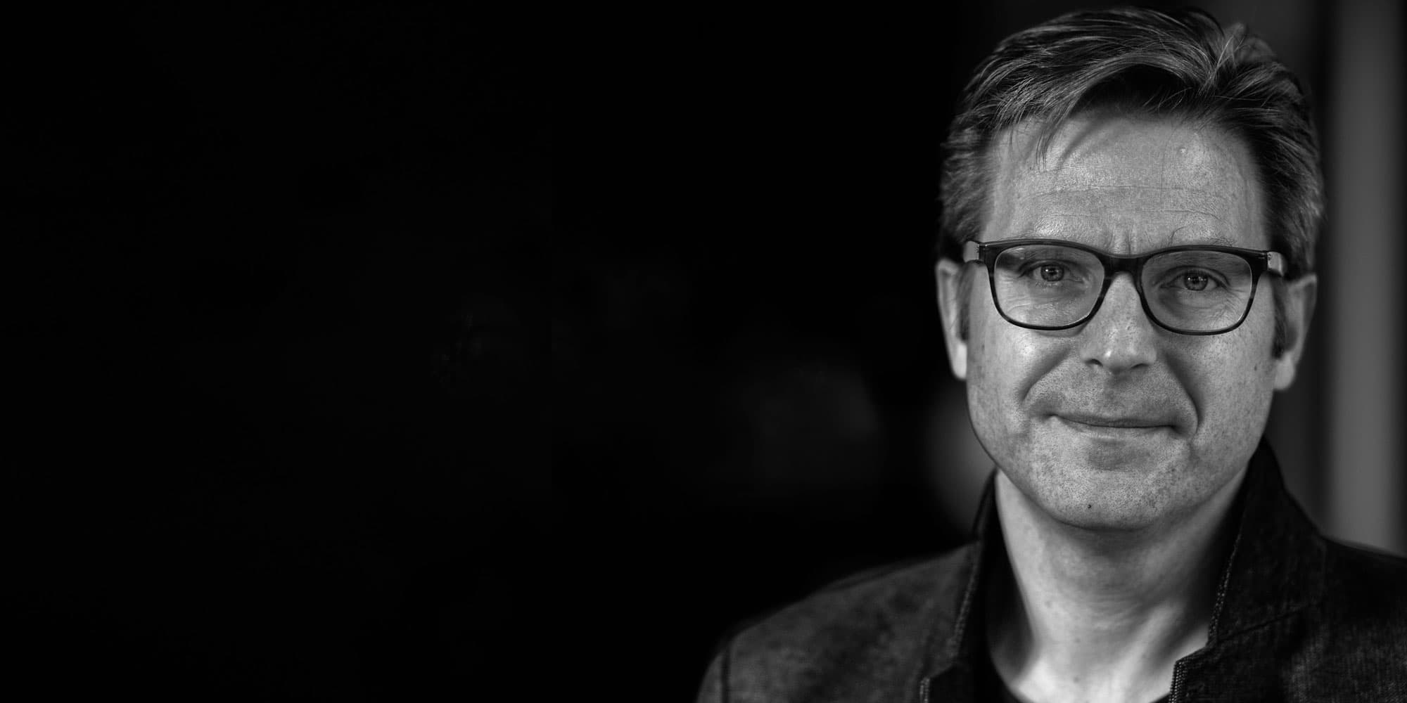 michael-peeters001magazinenew_1 Black-and-white portrait of Michael Peeters wearing glasses, against a dark background