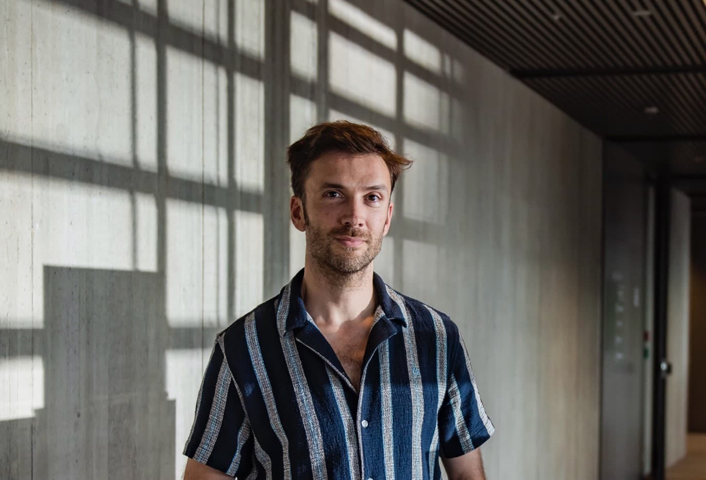 MichaelRademaker Portrait of Michaël Rademaker standing in a hallway with sunlight casting window shadows on the wall