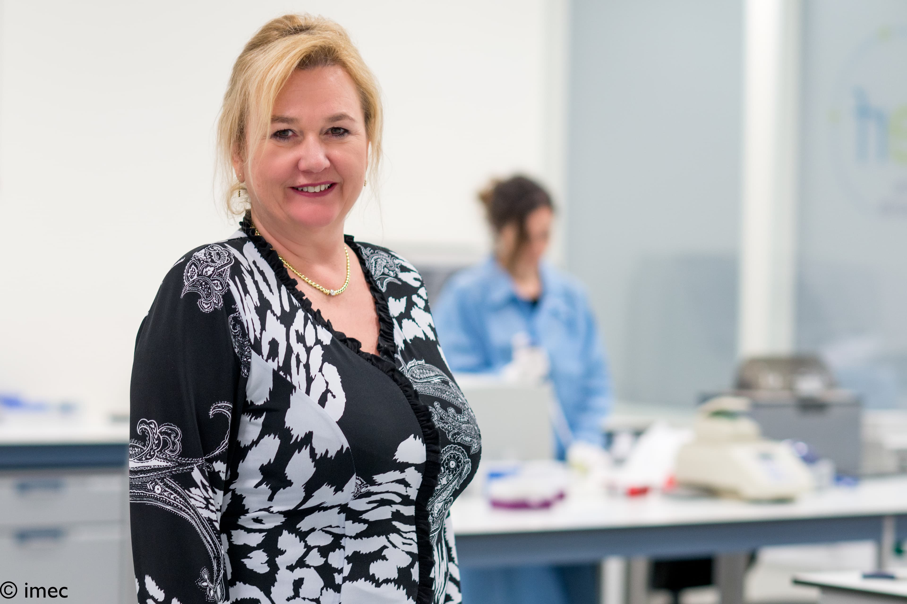 midiagnostics_5 Hilja Ibert stands in a clean lab, with a researcher blurred in the background.