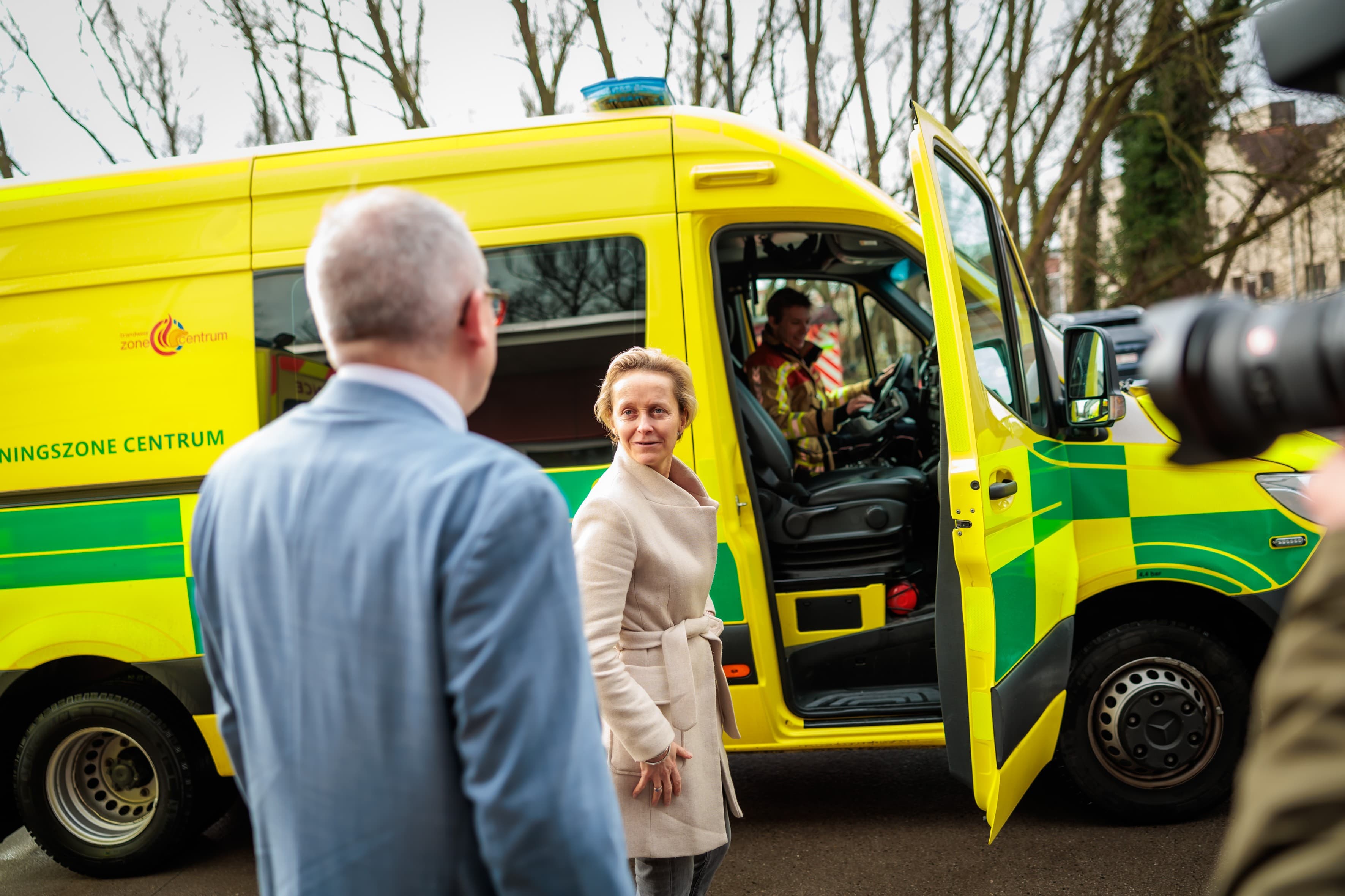 Ministers Officials spreken met een ambulanceverpleegkundige naast een geel-groene ambulance met de deur open