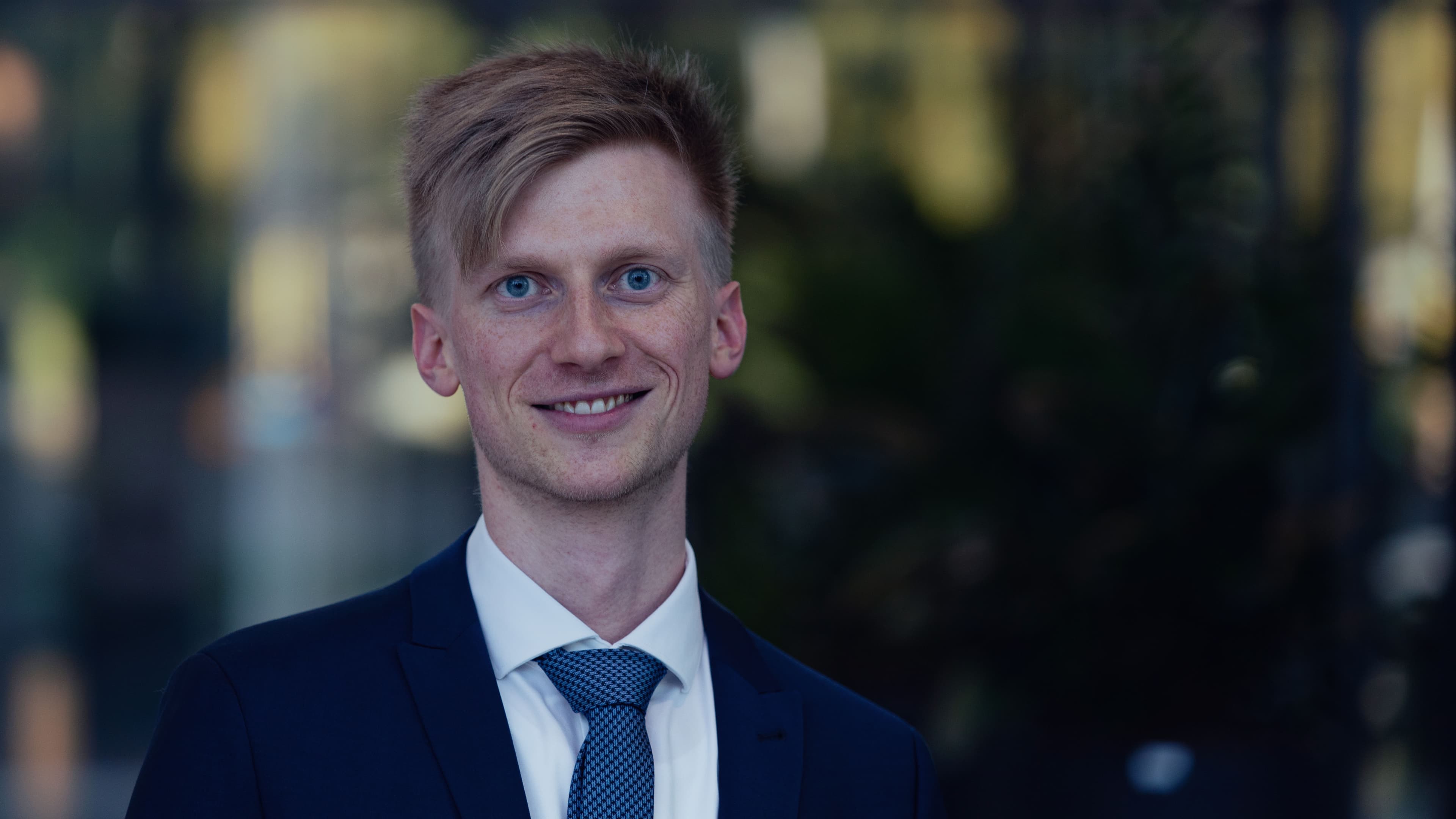 Moritz%20Brunion001 Portrait of Moritz Brunion in a suit and tie, smiling against a blurred outdoor background.