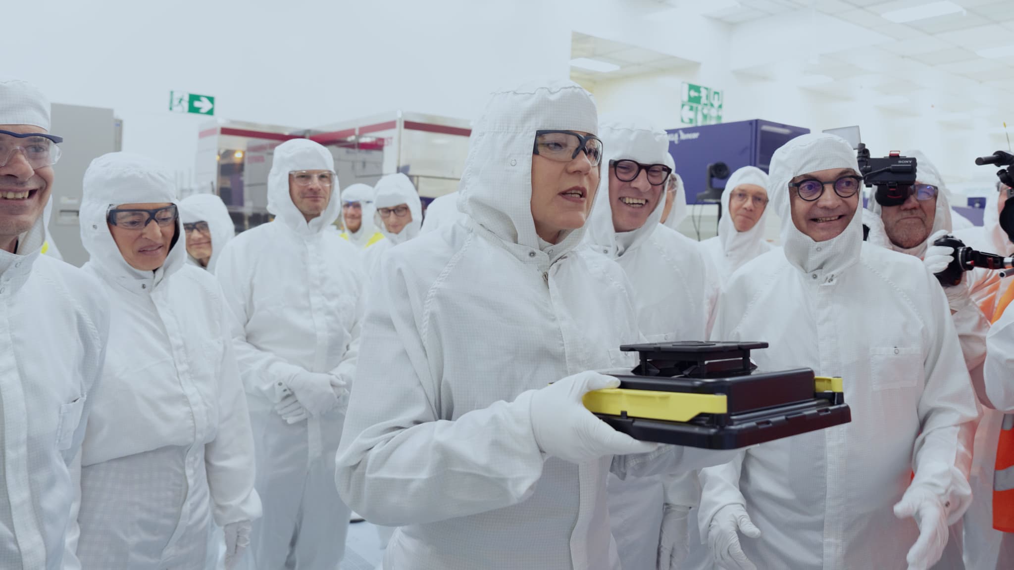 NANOIC6_maxHeight_1152_maxWidth_2048 European Commissioner Henna Virkkunen speaks in a cleanroom while holding a wafer carrier, surrounded by suited staff and cameras.