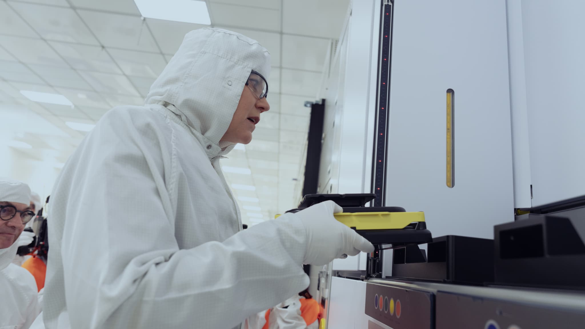NANOIC8_maxHeight_1152_maxWidth_2048 Researcher in a cleanroom handling equipment beside a large semiconductor machine
