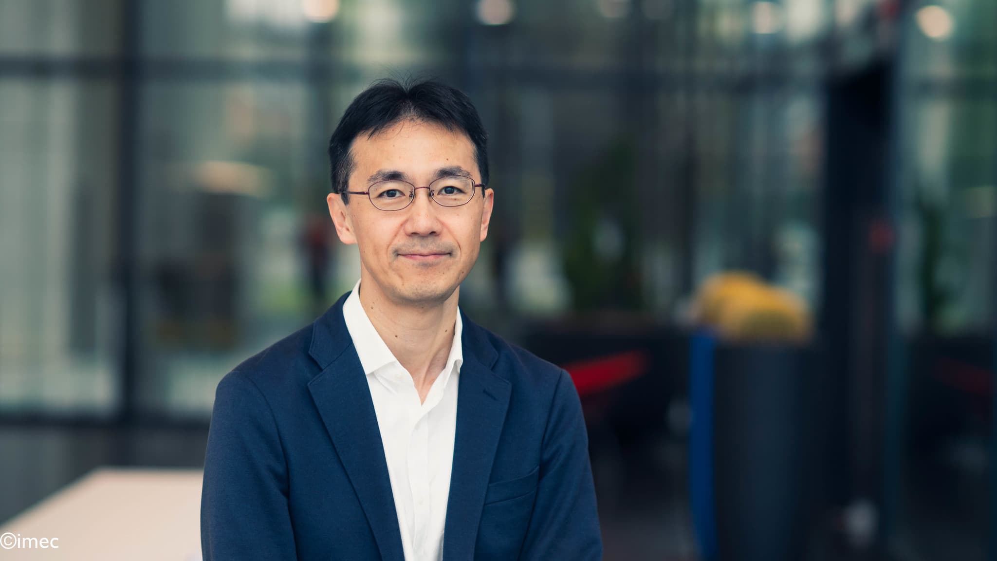 Naoto%20Horiguchi Portrait of Naoto Horiguchi in a navy blazer and glasses, standing in front of a blurred modern interior