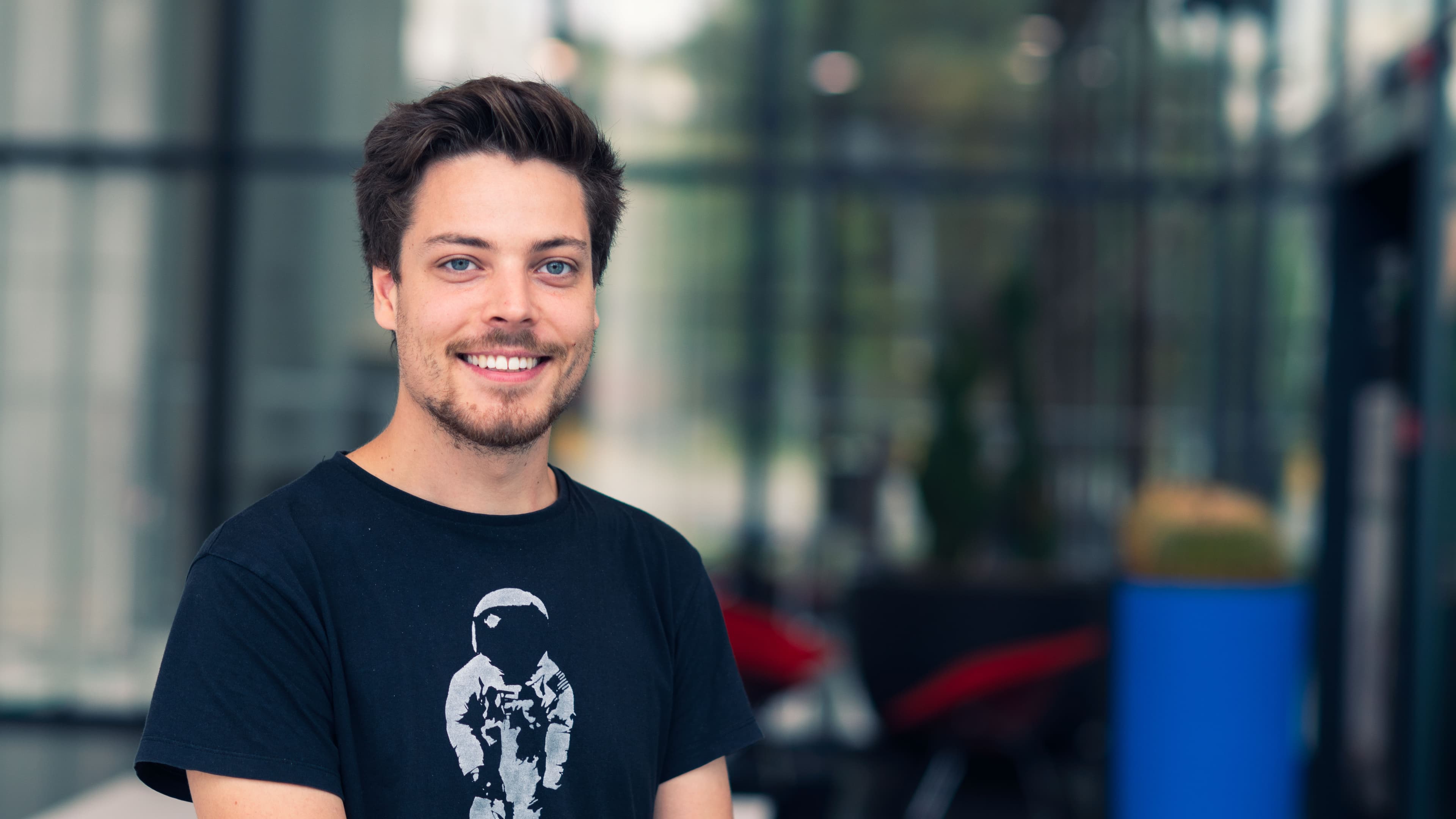 Nard.Dumoulin003 Smiling young man in a black T-shirt, posed in front of a blurred glass building