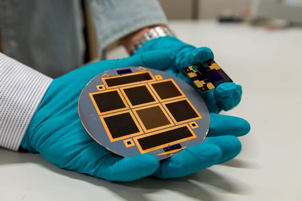 NVL220922_19110L_header Gloved hands holding a silicon wafer and a small photovoltaic test cell