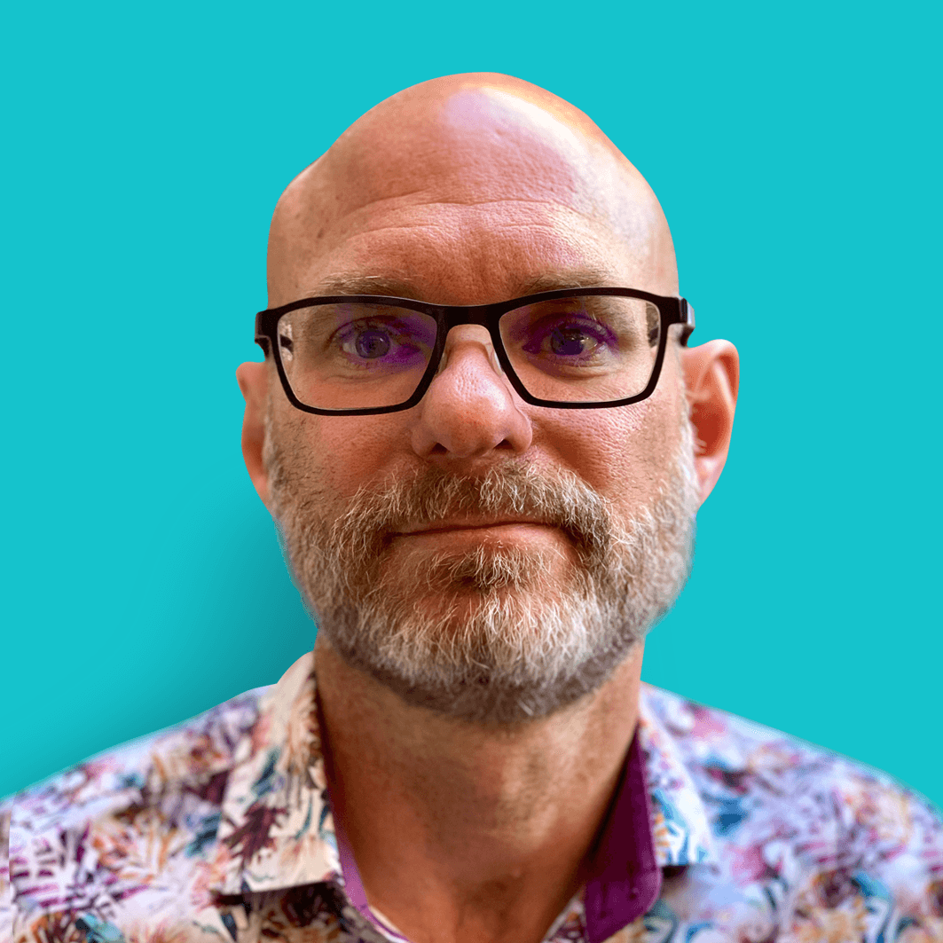 Oliver-Davies_SQ.UP_1 Portrait of Oliver Davies wearing glasses against a teal background