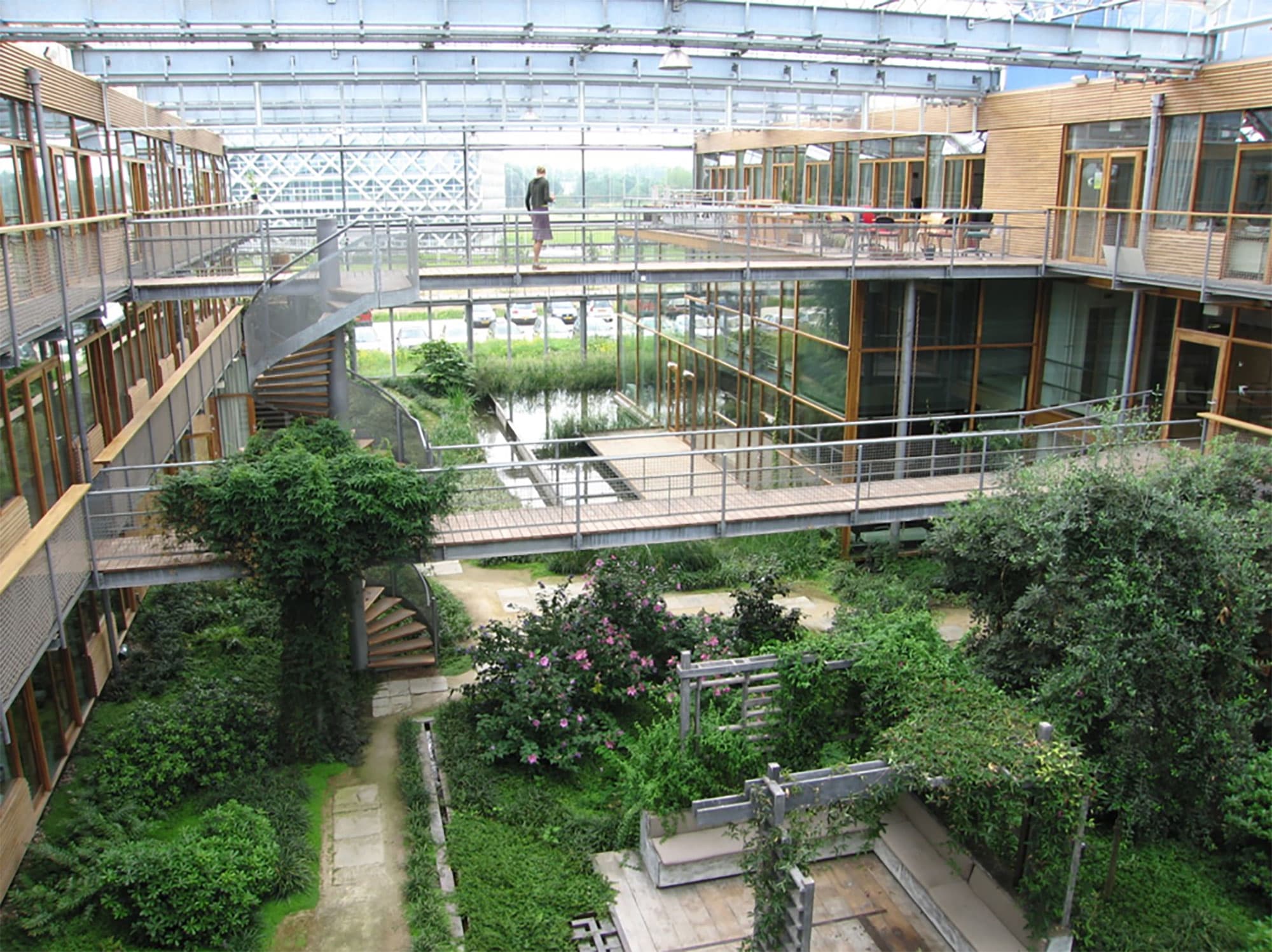 oneplanet_0 Atrium courtyard with glass walkways, greenery, and a person standing on the upper level of the OnePlanet Research Center