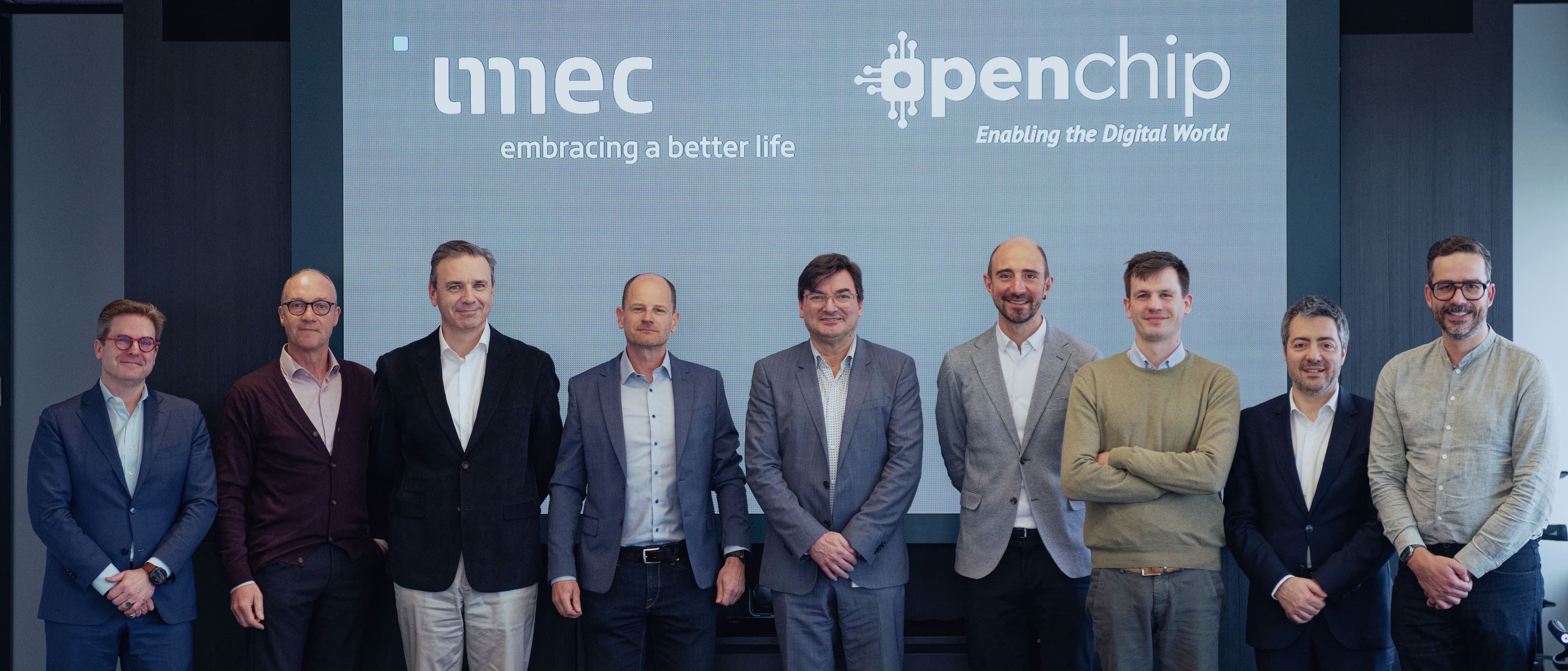 Open%20Chip00005 Group of eight men posing in front of an imec and Openchip backdrop at a partnership announcement