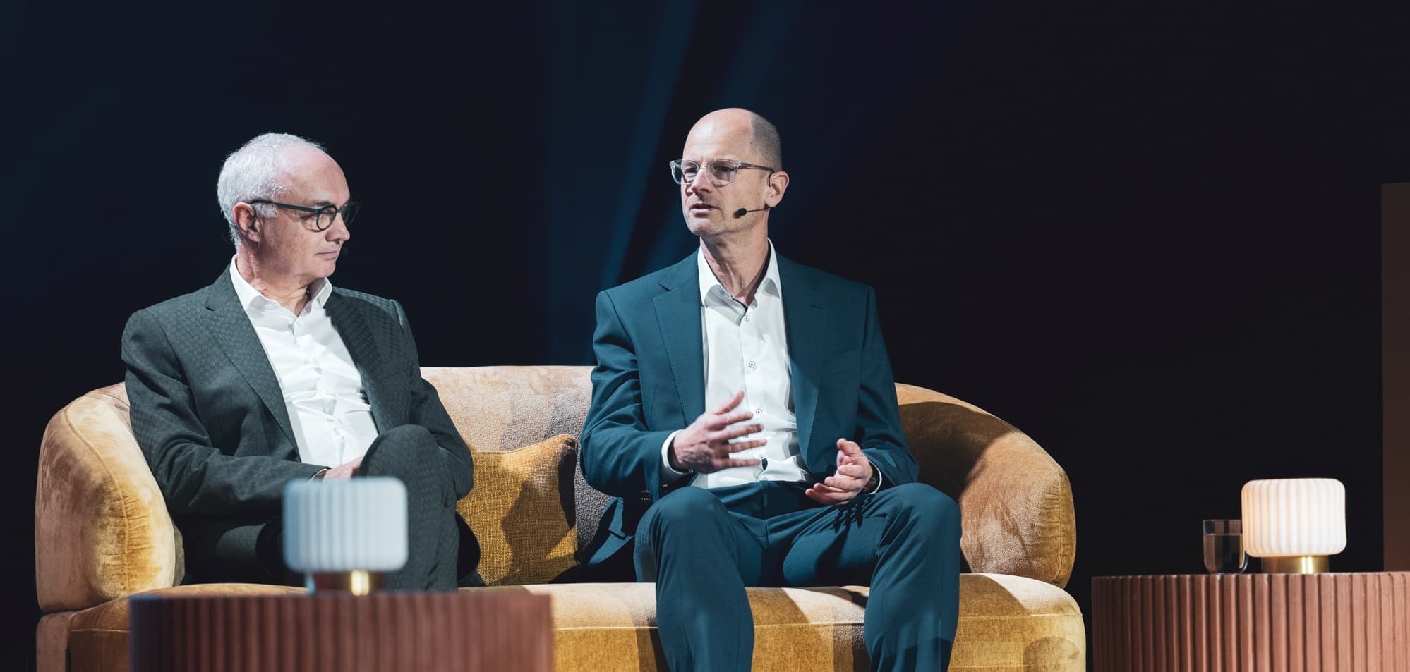 openminds2025-023-crop Two men in suits speaking on a stage during a panel discussion