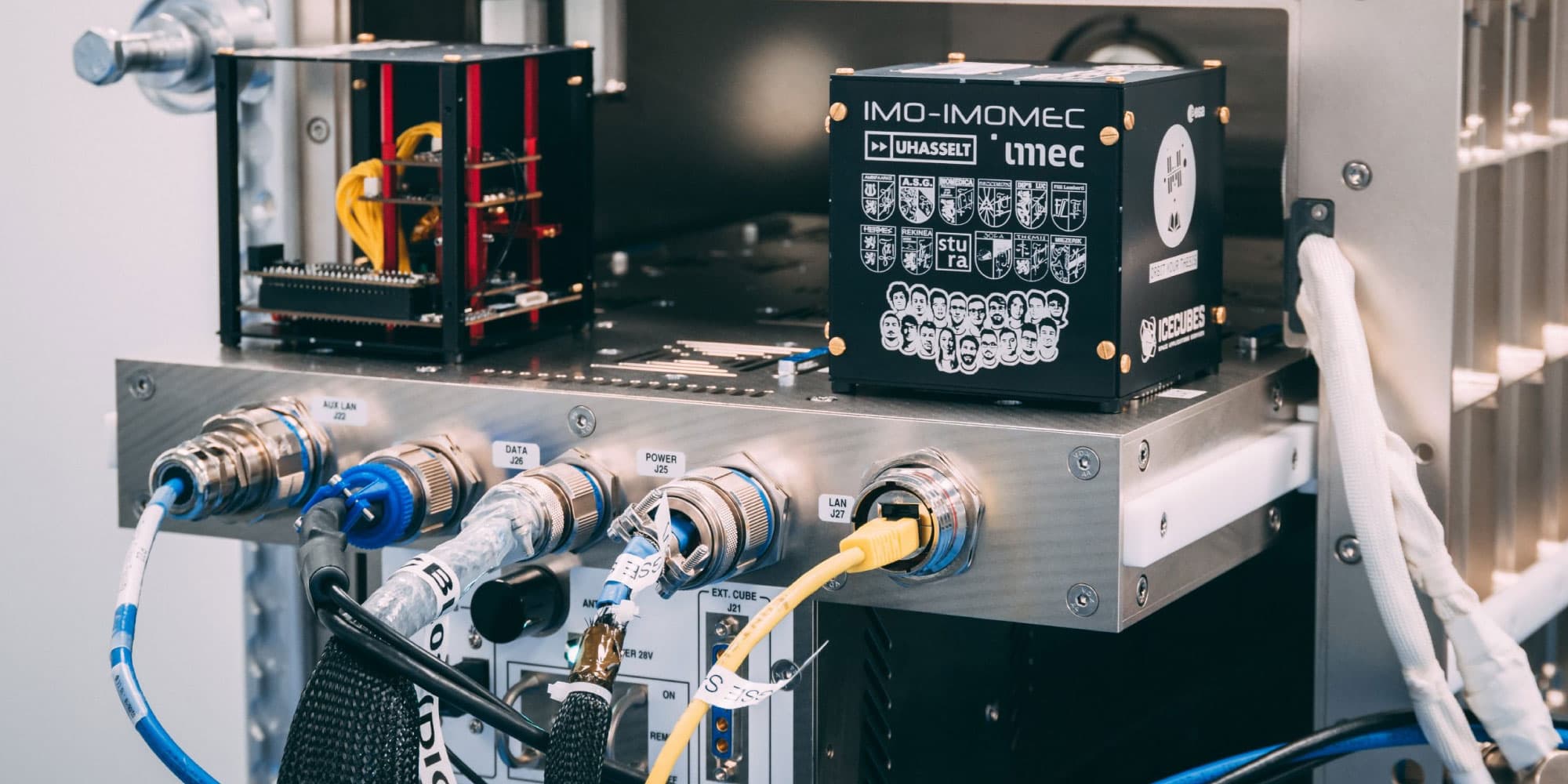 OSCARqube OSCAR-QUBE cube satellite hardware with imec and UHasselt logos, mounted among connected cables and lab equipment