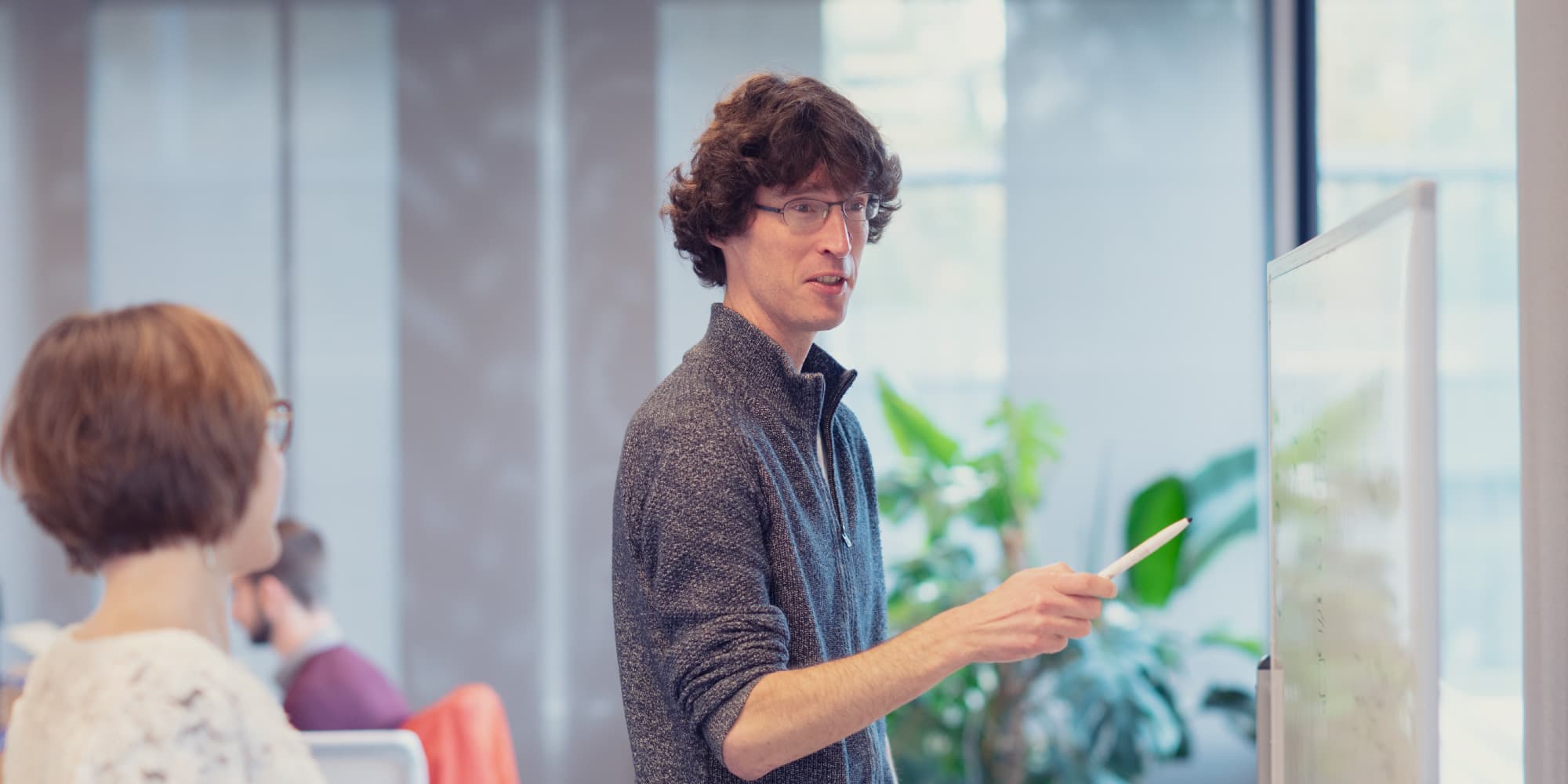 Our-future-starts-with-you-Wim-Yedema Colleague presenting at a whiteboard in a meeting room, with coworkers listening nearby.