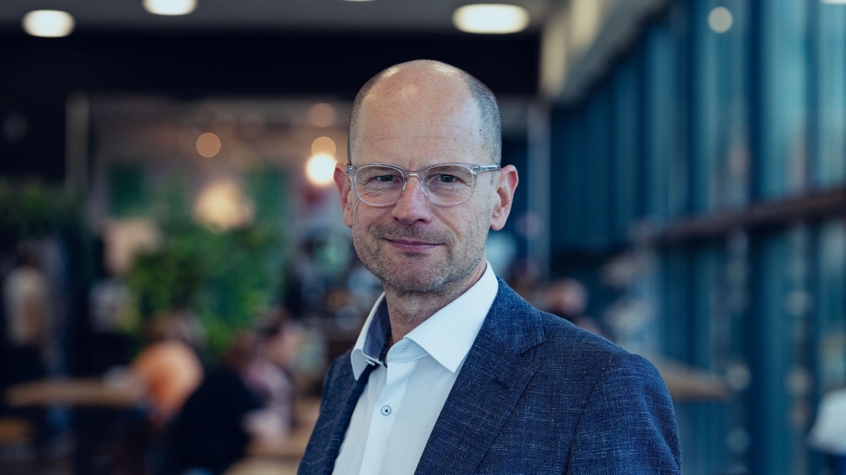 Patrick%20Vandenameele Portrait of Patrick Vandenameele in a business suit and glasses, standing in a modern office setting